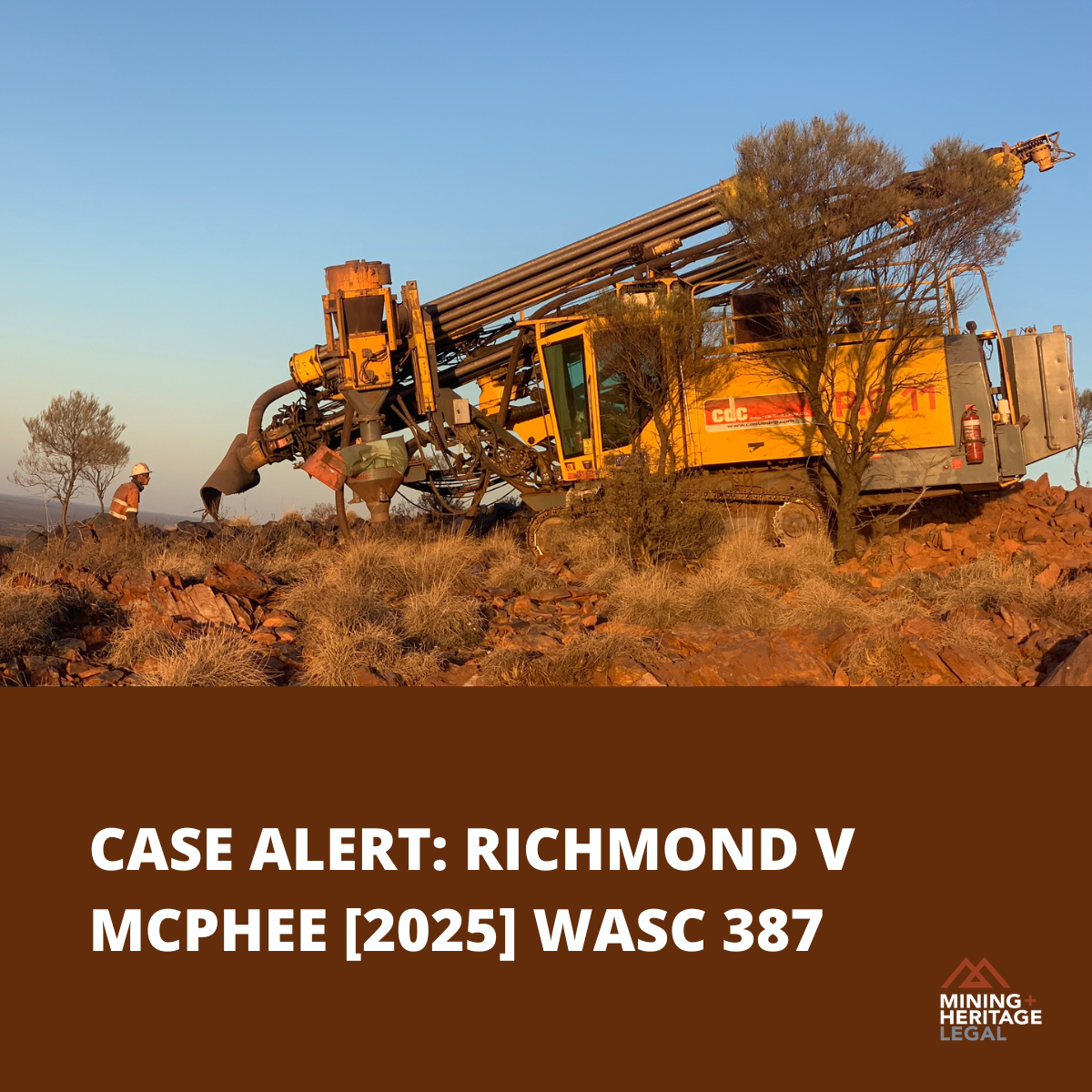 An orange drilling machine in a rocky, dry landscape with sparse trees, a worker in safety gear nearby, under a clear blue sky.