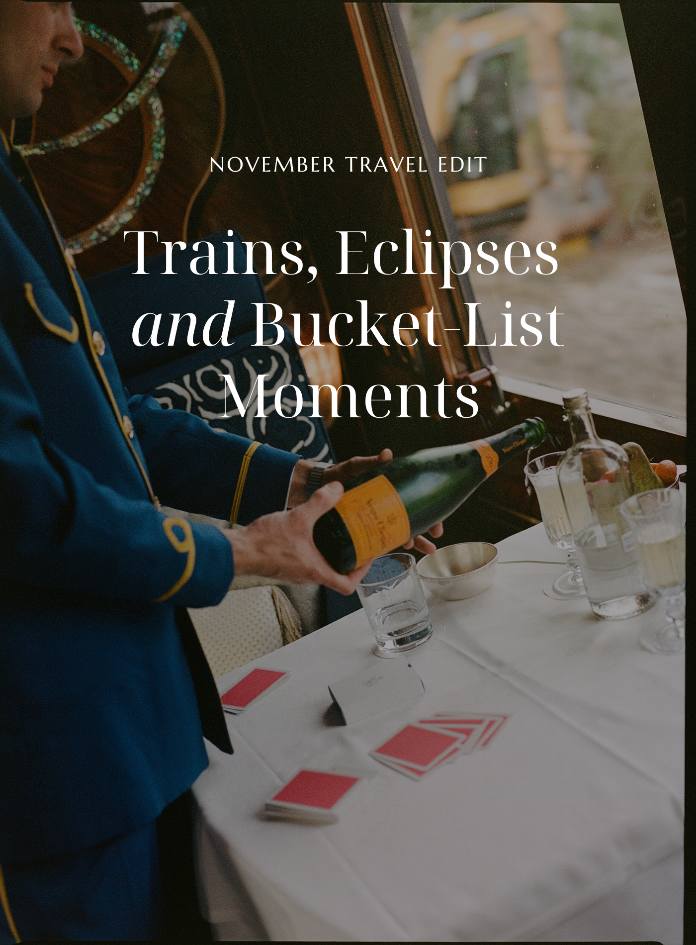 A person in a blue suit opening a bottle of champagne at a table with playing cards, glasses, and bottles inside a train.