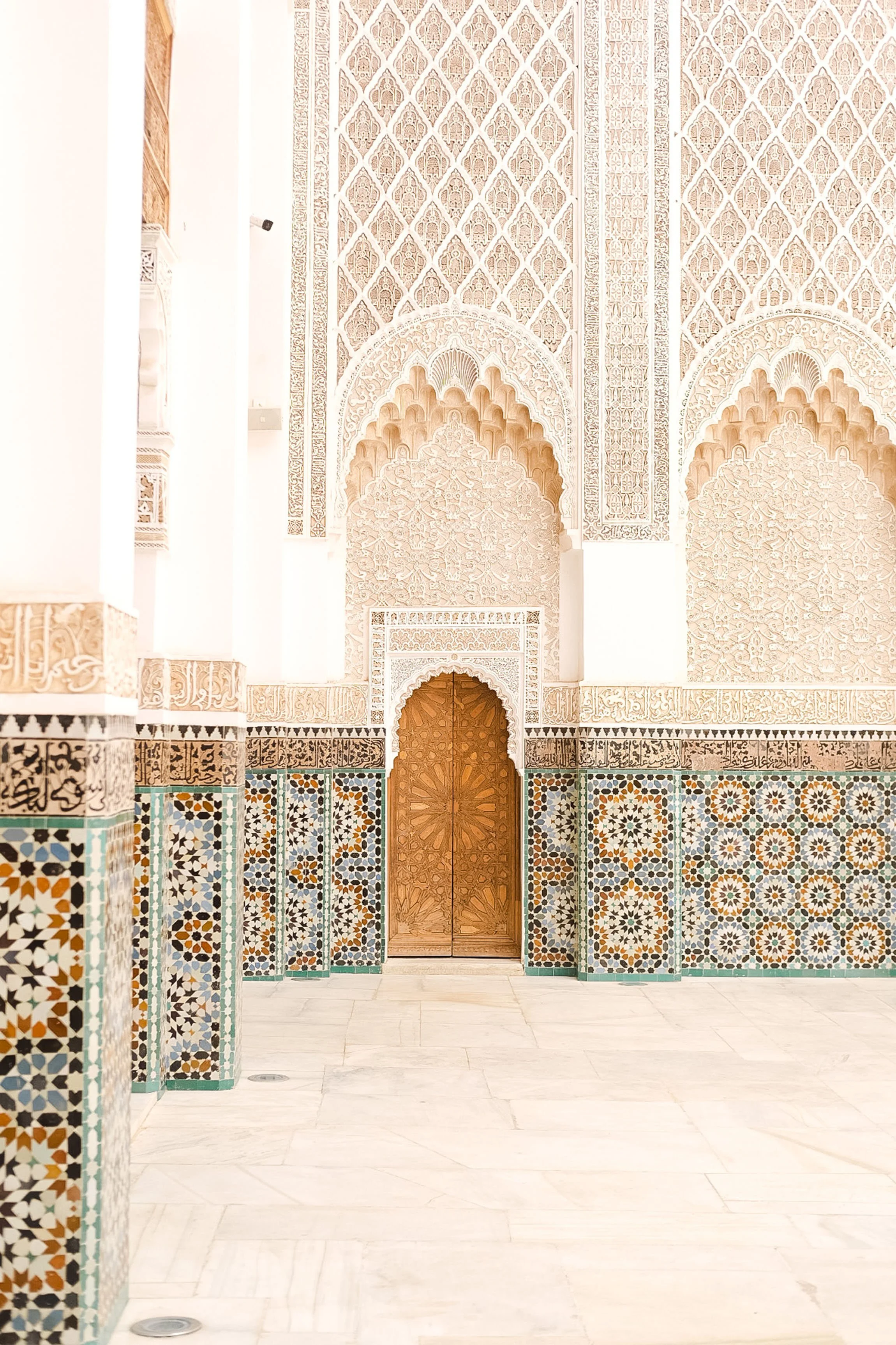 Detailed view of a Moroccan interior with ornate white plaster wall carvings, colorful tile work, and a wooden door.