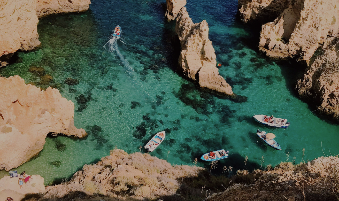 A group of boats floating in clear turquoise water among rocky cliffs at a beach.