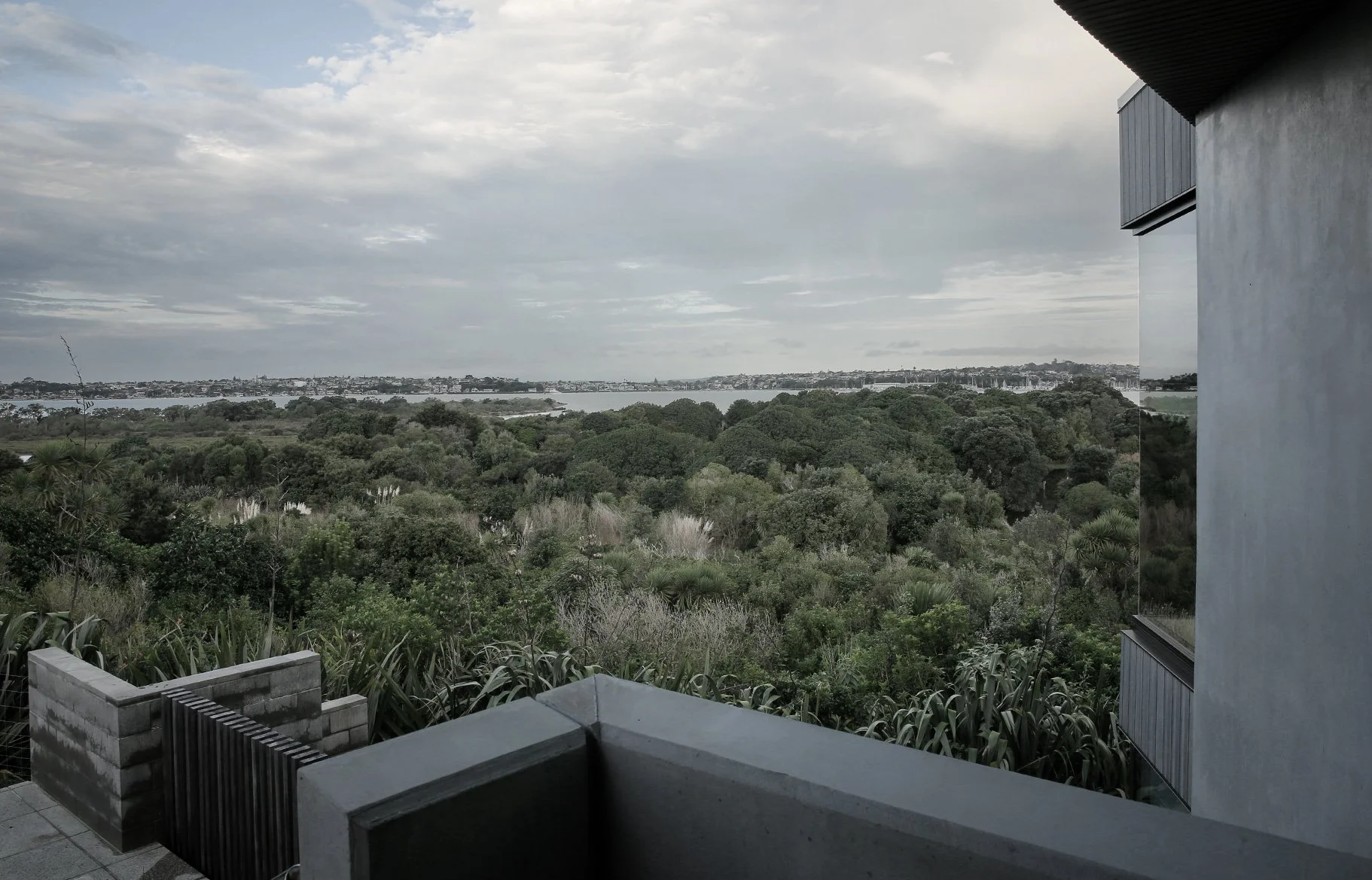 View of a lush green landscape with trees and a body of water in the distance, seen from a balcony or terrace with modern architecture.