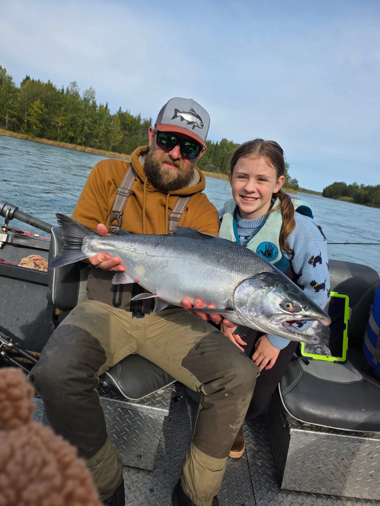 An adult and child holding a salmon together in a fishing boat