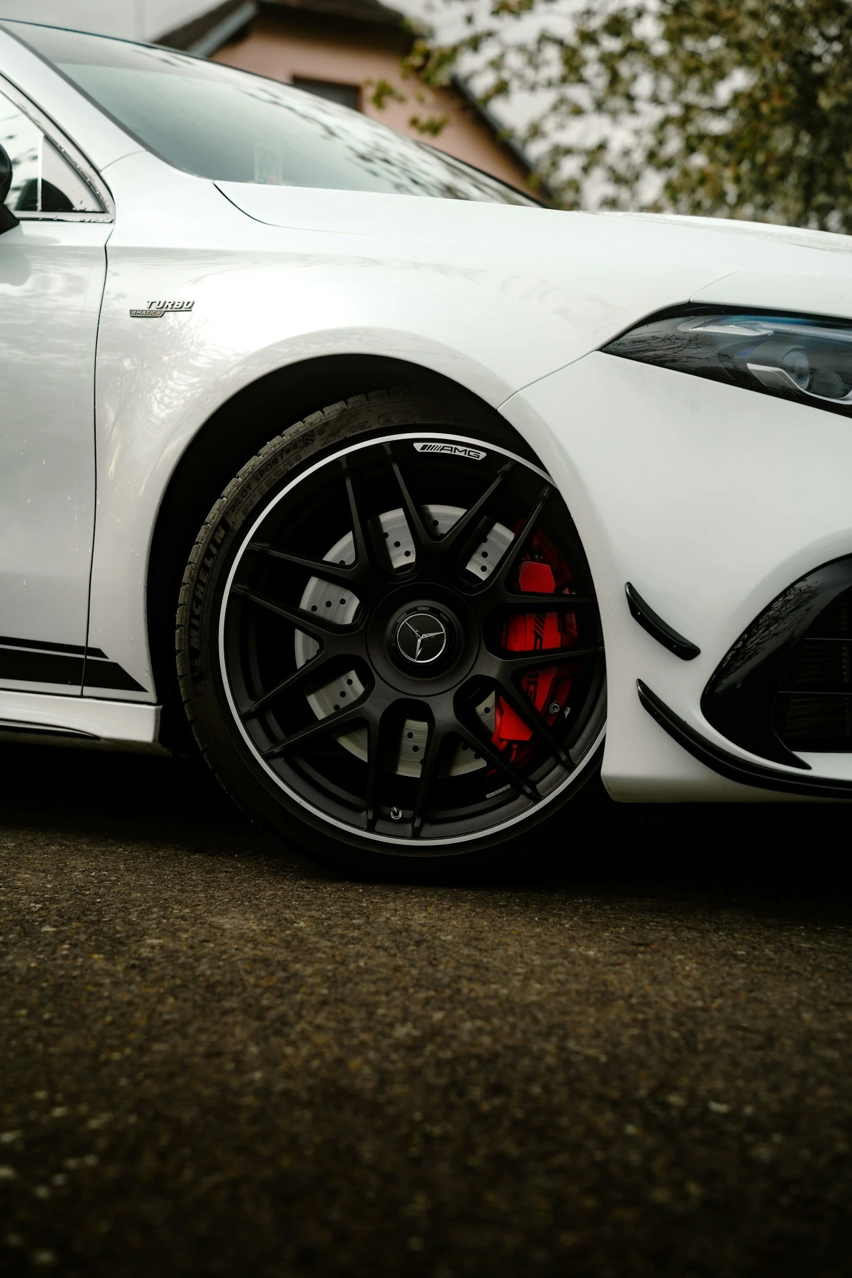 Close-up of front part of a white Mercedes-Benz AMG car, featuring black AMG wheels with red brake calipers, parked on an asphalt surface.
