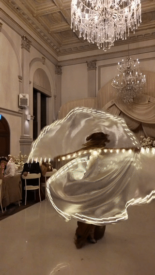Person twirling with a shiny, reflective umbrella in an elegant banquet hall decorated with chandeliers and drapes.