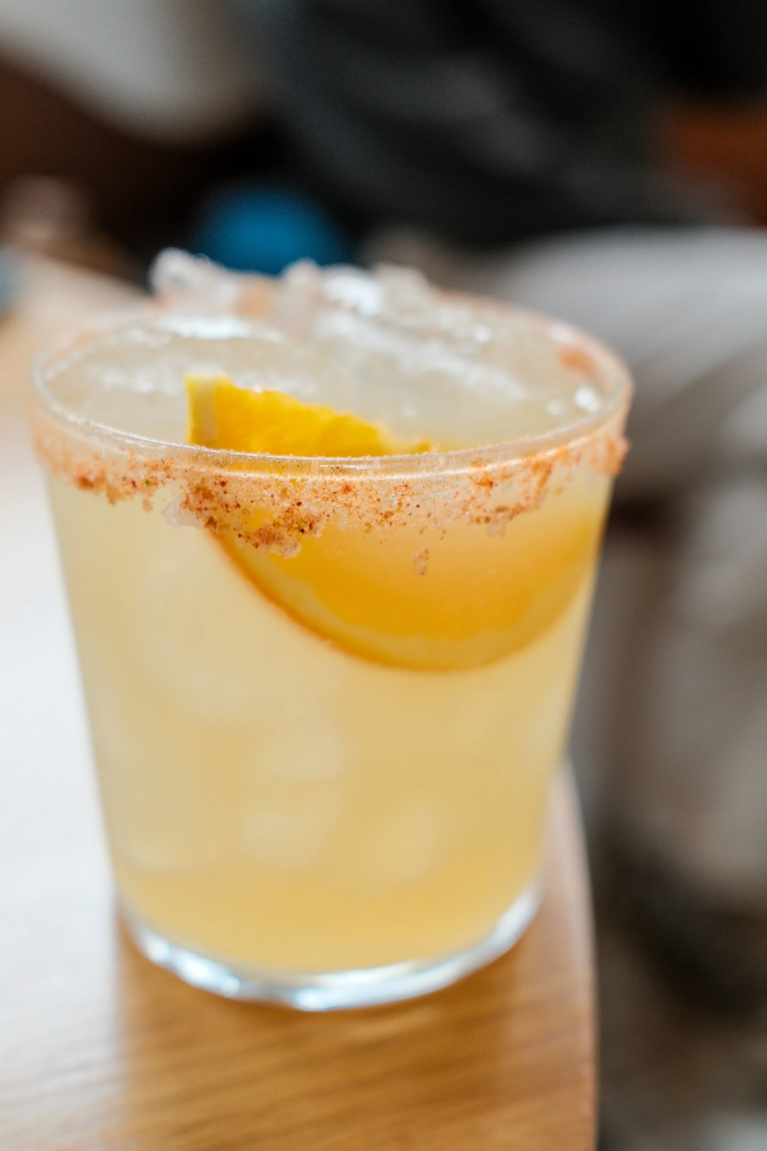 Close-up of a margarita cocktail in a transparent glass with a salted rim and lime wedge garnish, placed on a wooden surface.