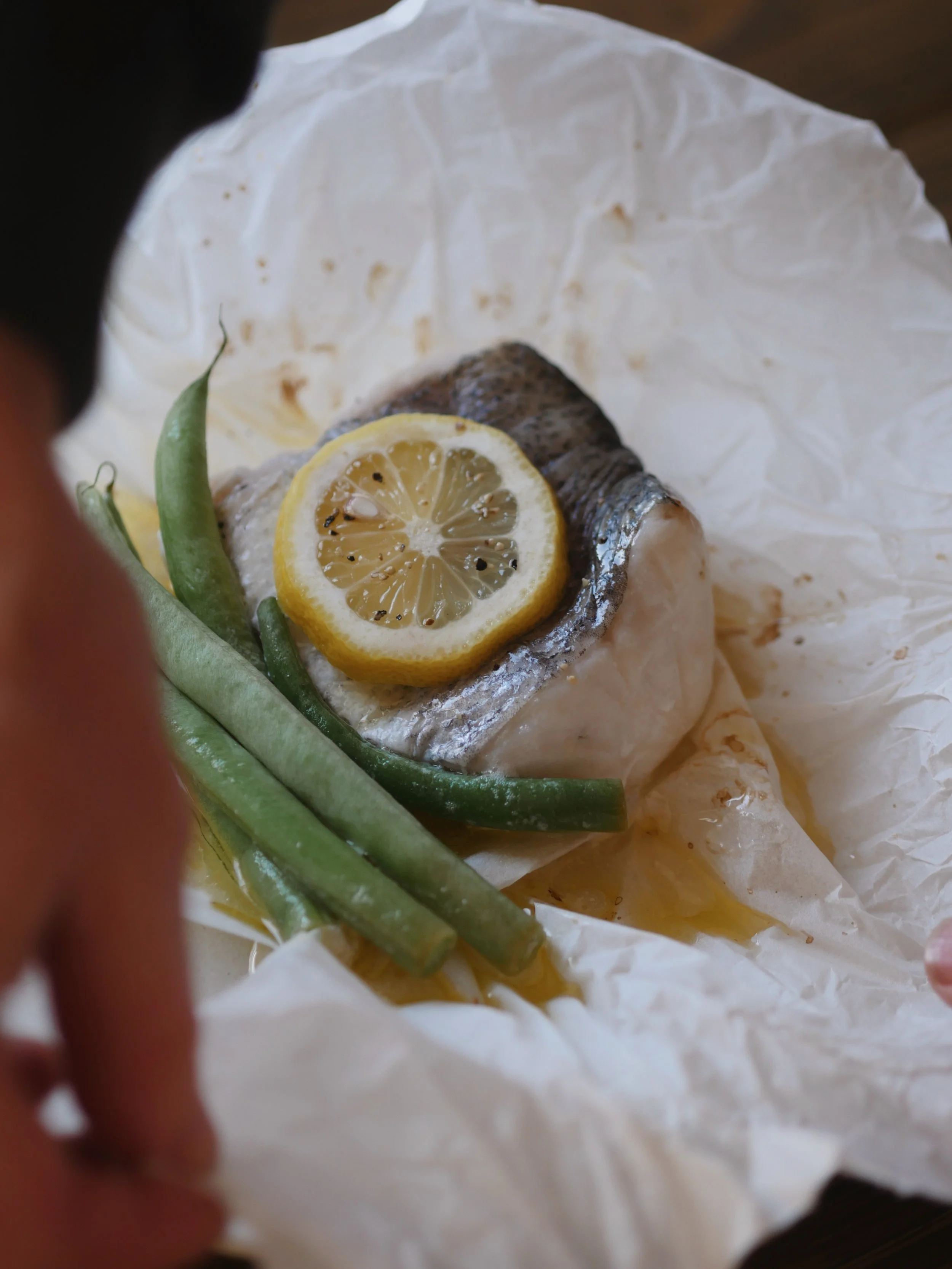 Fresh fish with lemon slice and green beans on crumpled white parchment paper.