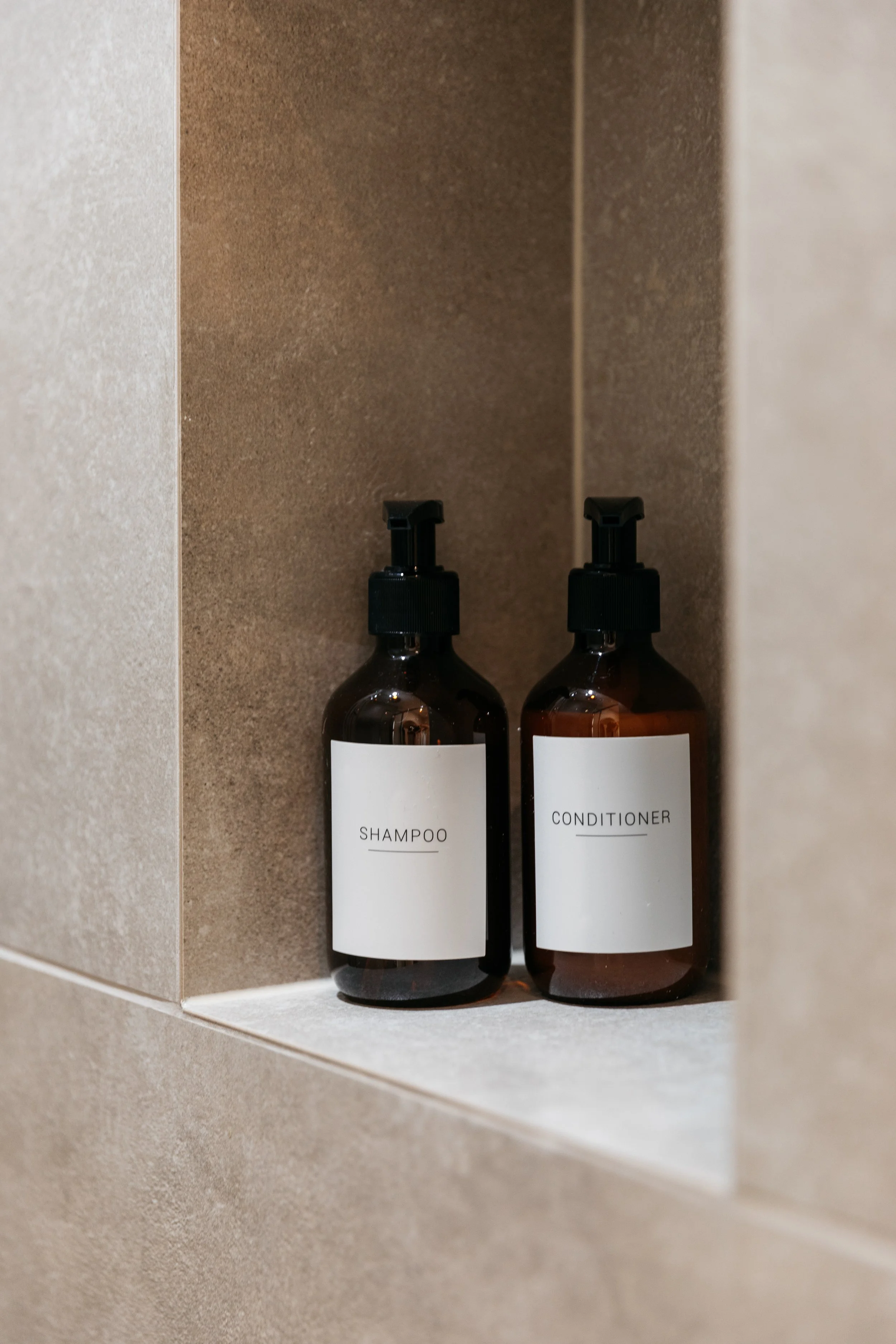 Dark amber bottles labeled shampoo and conditioner in a shower shelf.