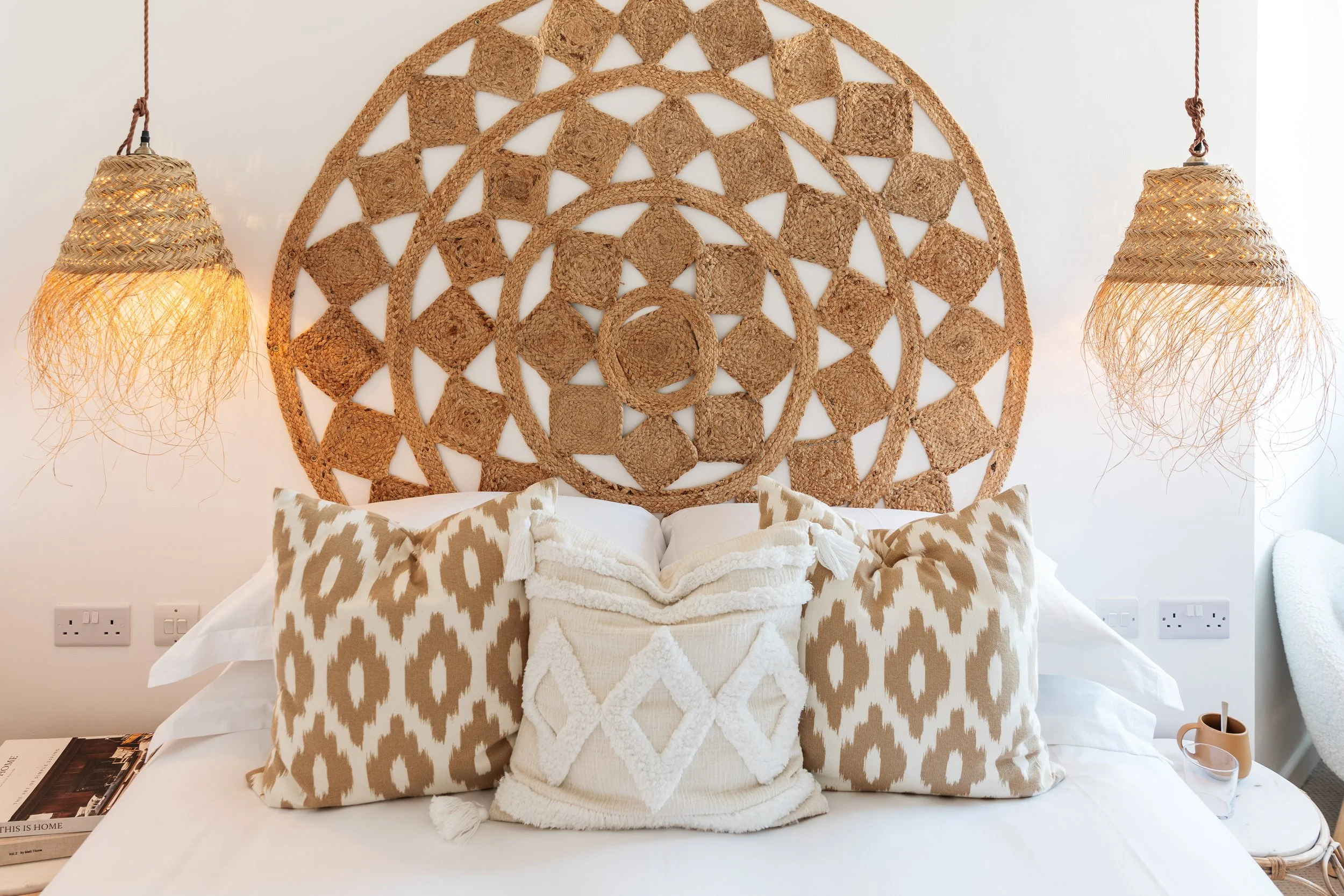 Decorative bedroom with woven rattan headboard, beige and white pillows, and two hanging woven pendant lights.