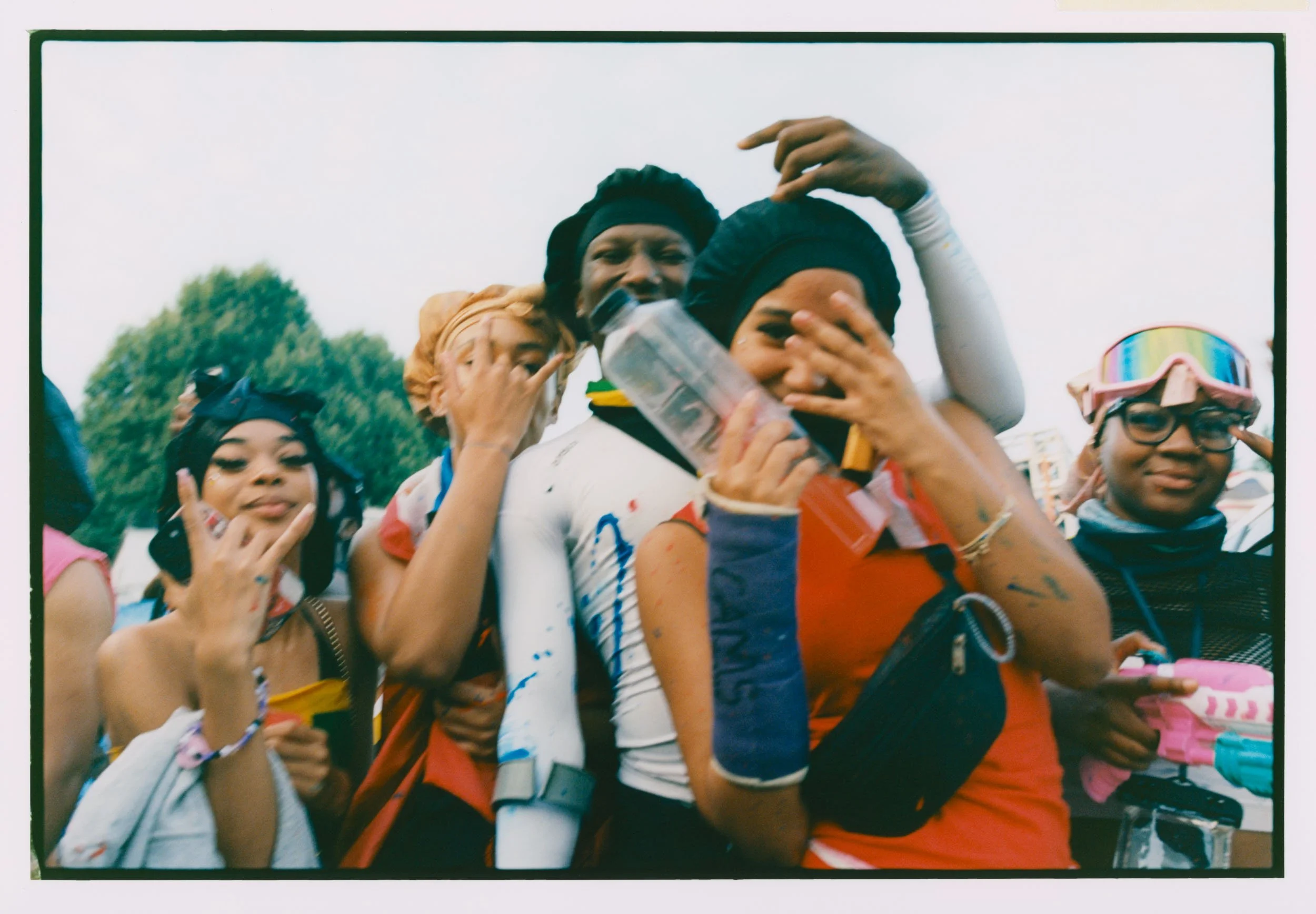 A group of young women wearing colorful sportswear, some with goggles and headbands, celebrating and posing happily at an outdoor event, with trees and other participants visible in the background.