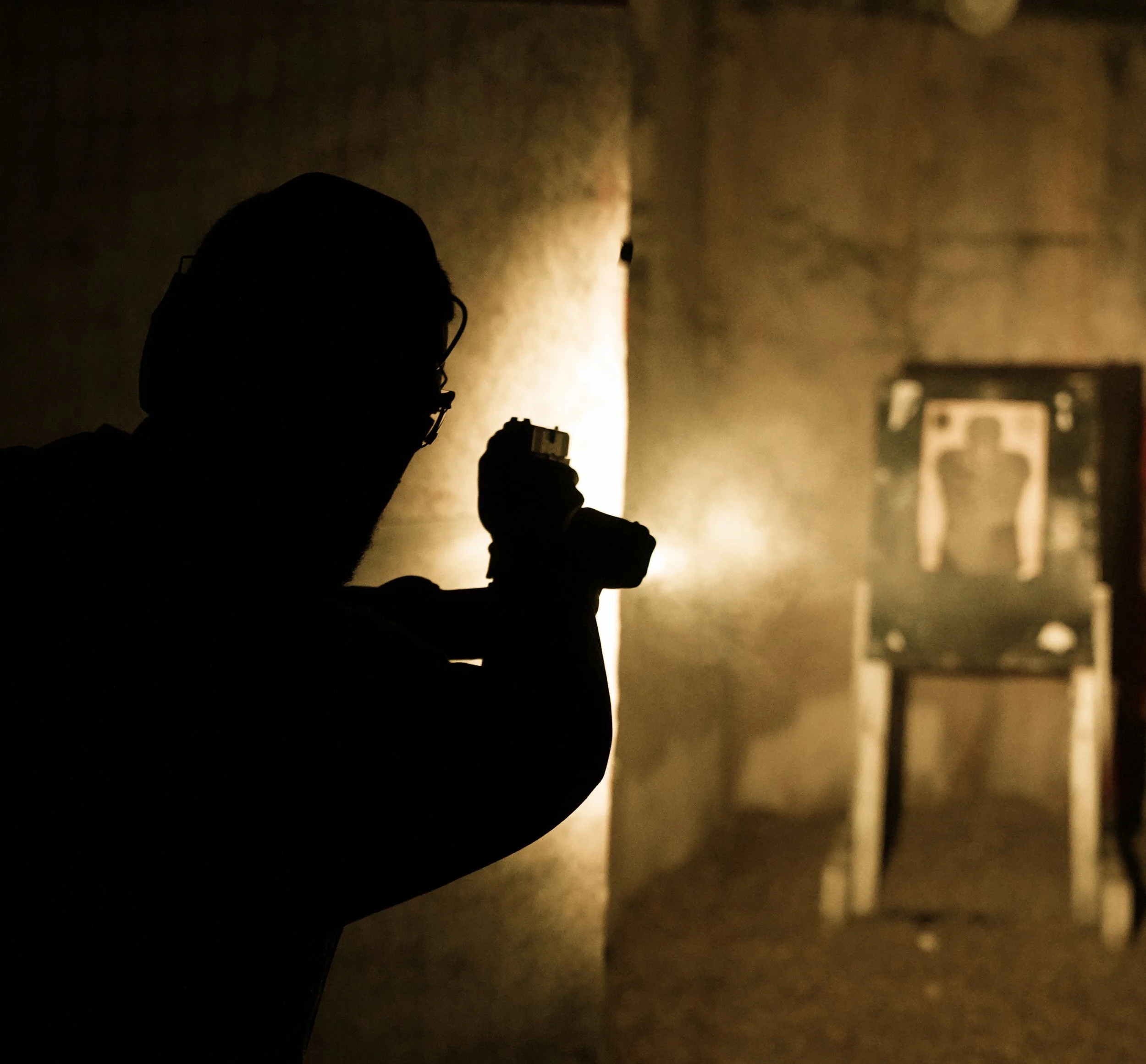 Silhouette d'une personne s'entraînant au tir dans une pièce sombre, visant une cible au fond.