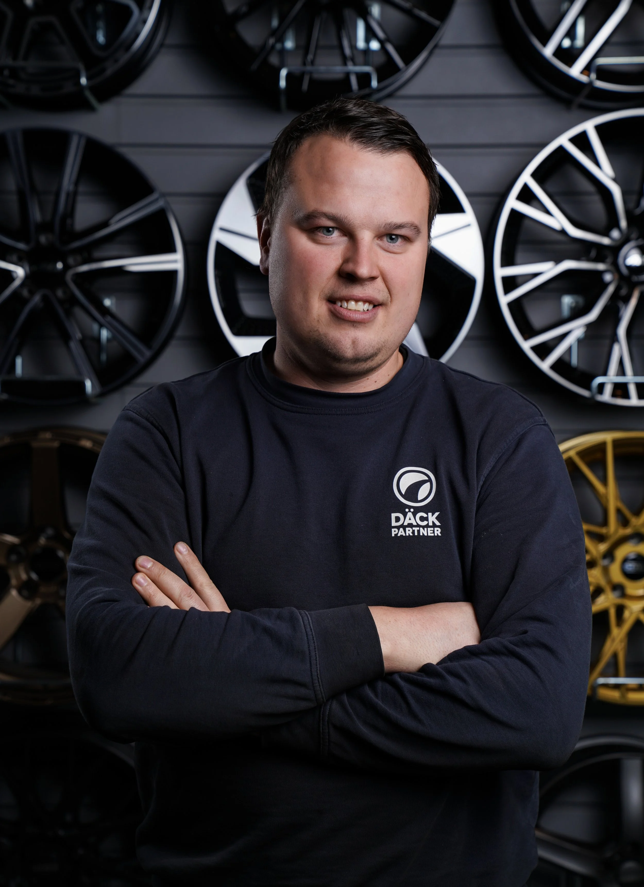 En man med mörkt lockigt hår, skägg, glasögon och näsring, som tittar åt sidan, sittande i ett rum med växt i bakgrunden.