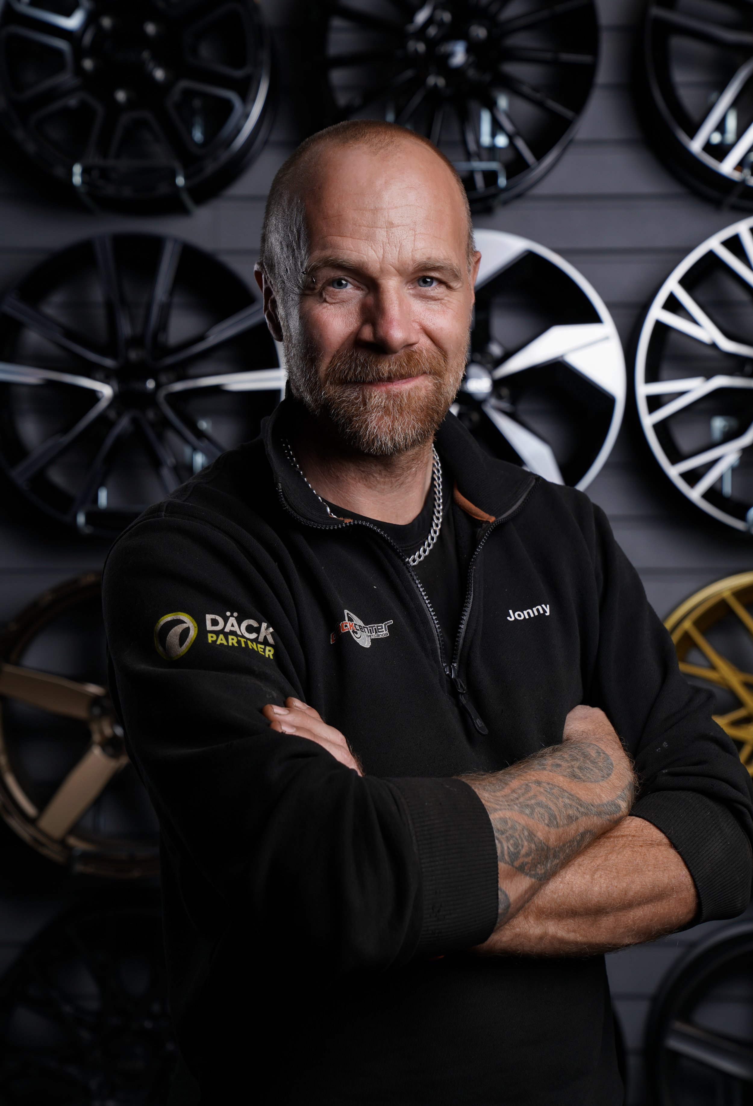 En leende kvinna med kort svart hår, iklädd en blå topp, står bland gröna växter.