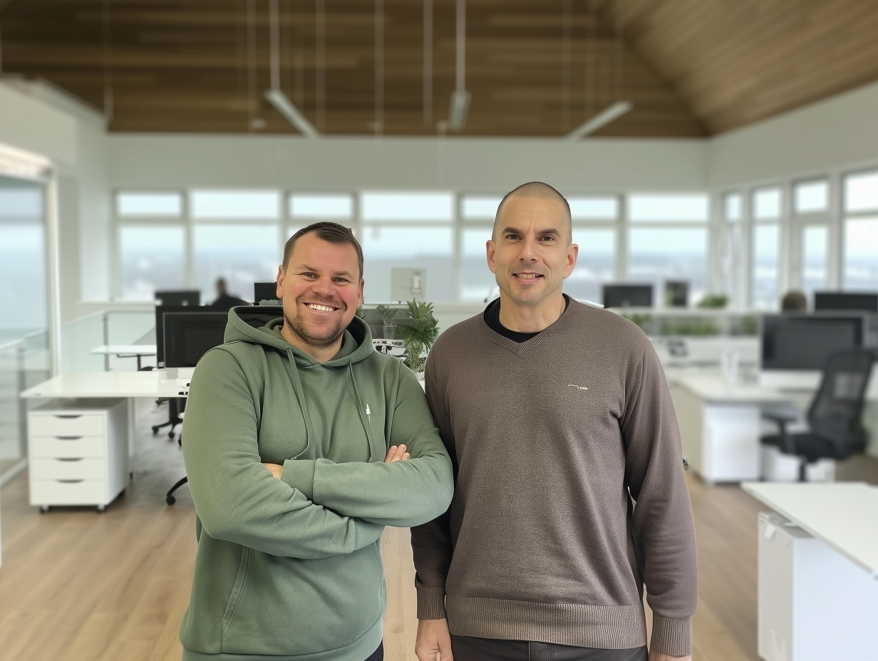 Zwei lächelnde Männer stehen in einem modernen Büro vor großen Fenstern, die einen Stadtblick bieten.