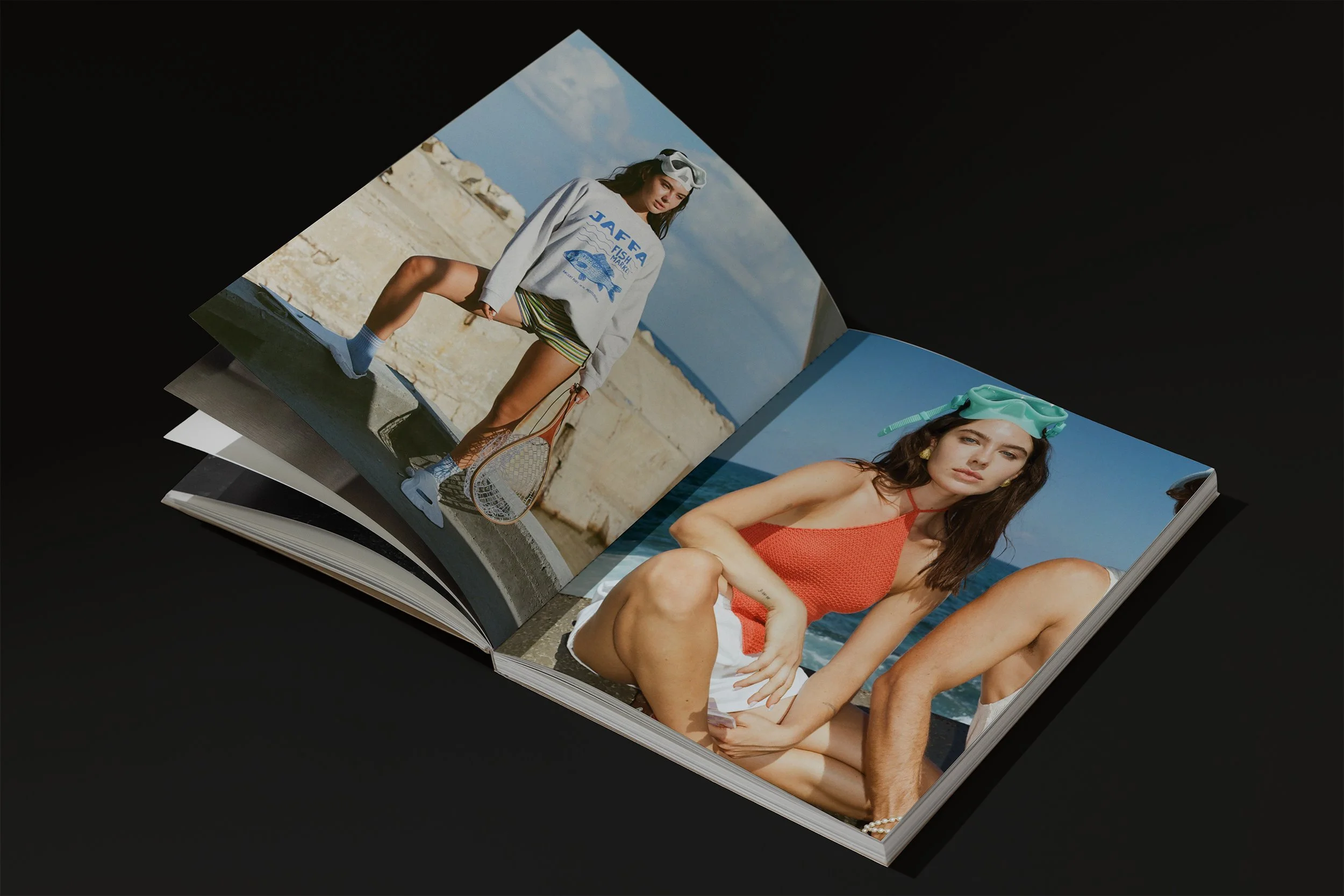 Open magazine displaying two photos of women at the beach. The woman on the left is wearing a gray sweatshirt, striped shorts, socks, sneakers, and holding a tennis racket. The woman on the right is wearing a red swimsuit, white shorts, and a snorkeling mask on her head.