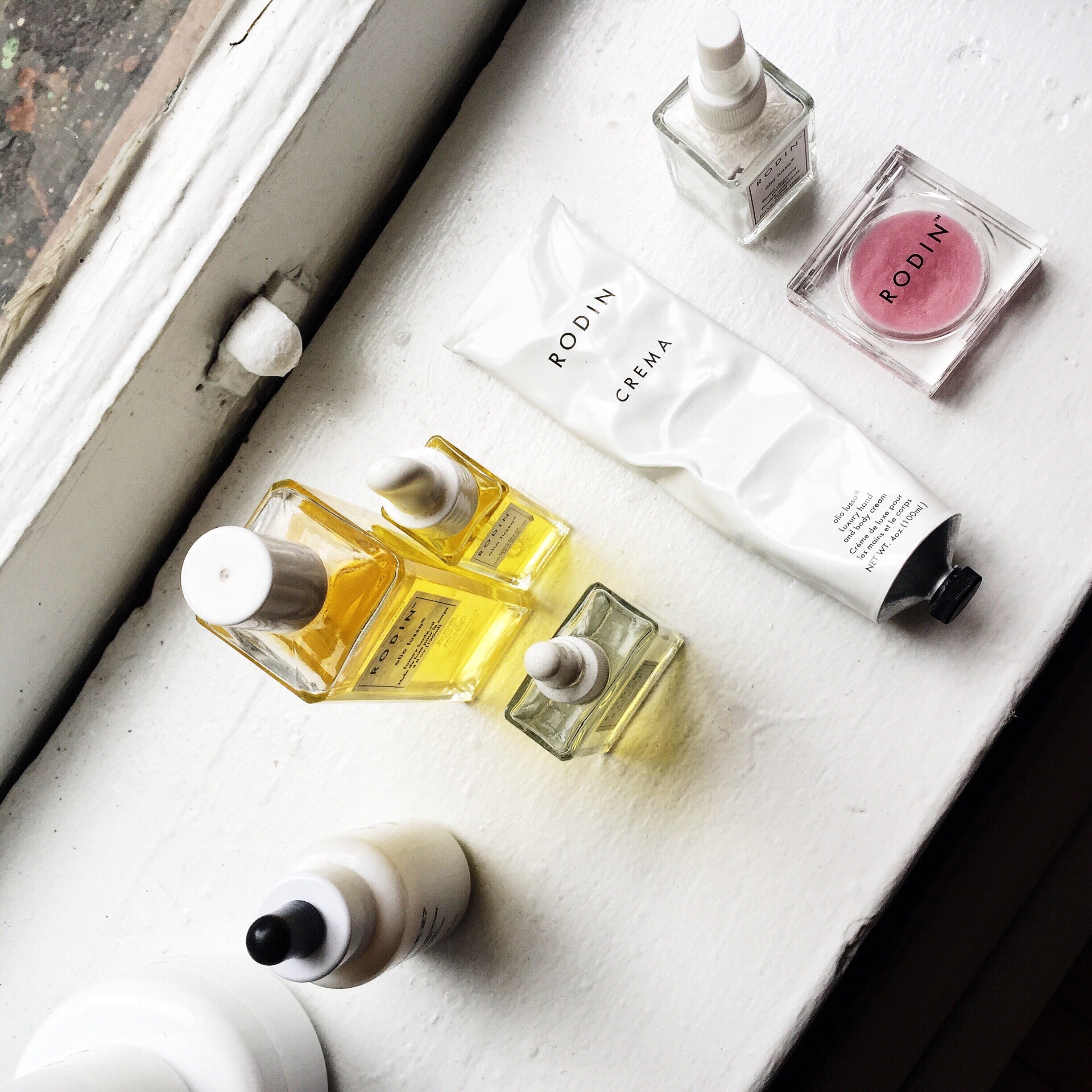 Collection of skincare and beauty products on a windowsill, including bottles of oils, creams, a pink container, and a white tube.