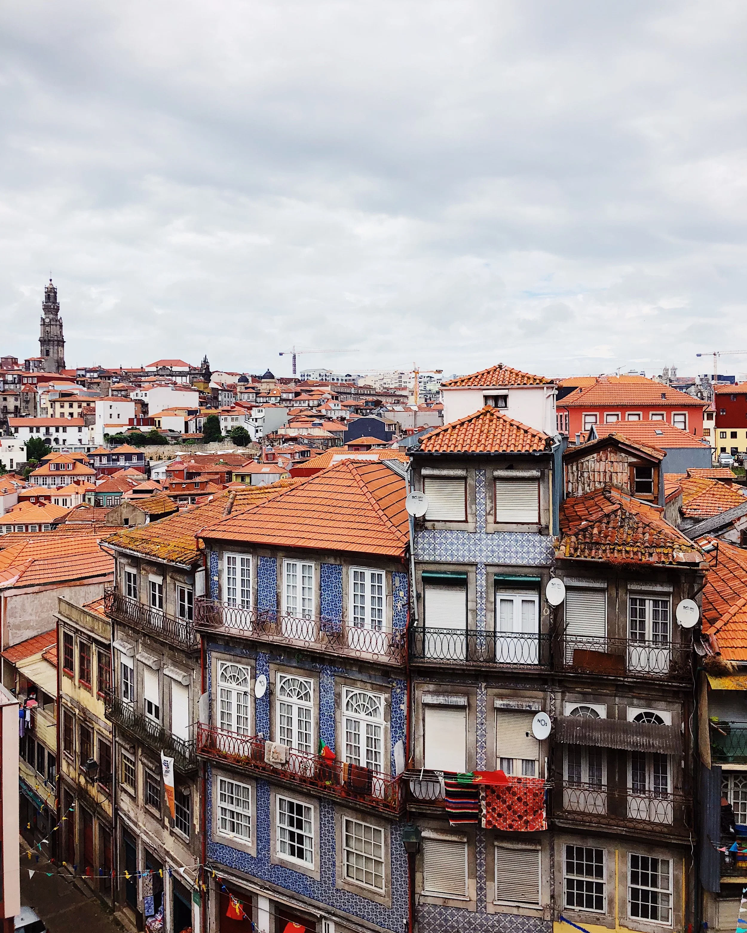 View of a cityscape with old buildings with red roofs, some with balconies and satellite dishes, and a skyline with various historic and modern structures under a cloudy sky.