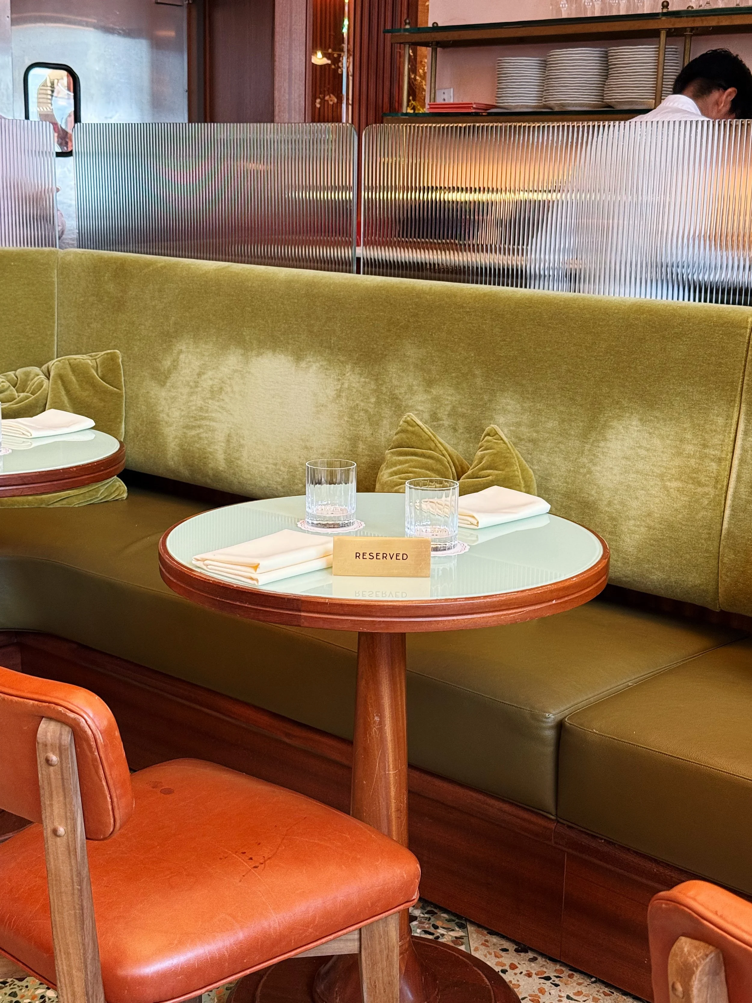 Empty restaurant table with reserved sign, two glasses of water, and folded napkins, surrounded by brown and green seating.