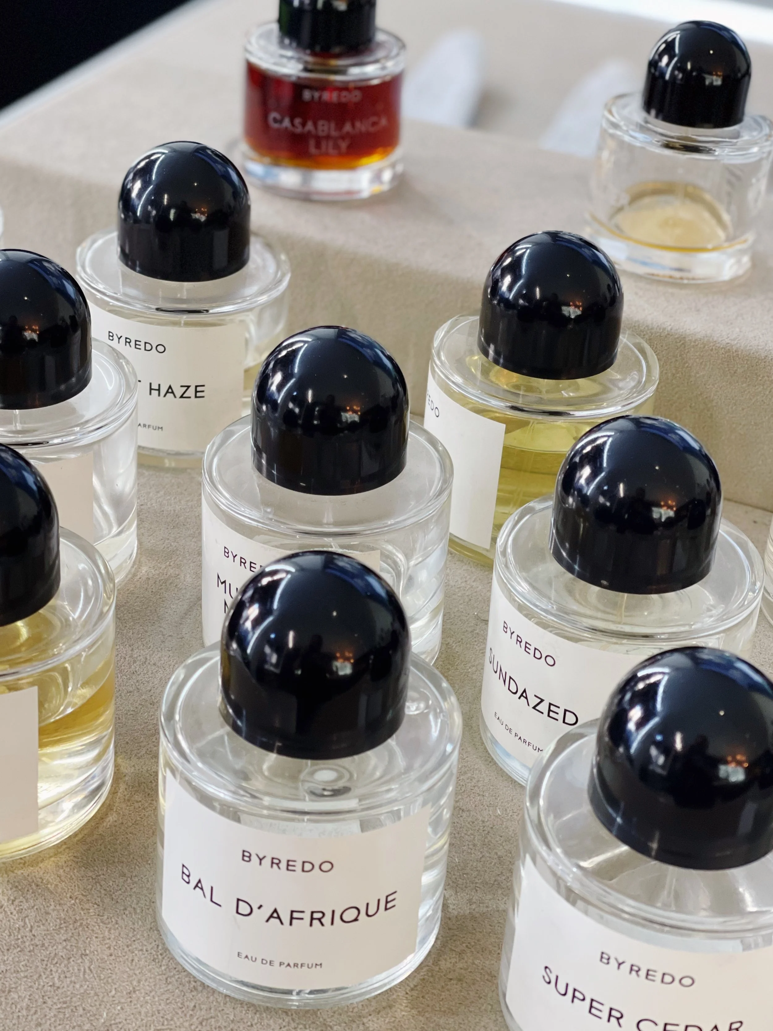 Collection of Byredo perfume bottles displayed on a beige surface, with some bottles labeled Bal d'Afrique, Super Cedar, Fremont and others.