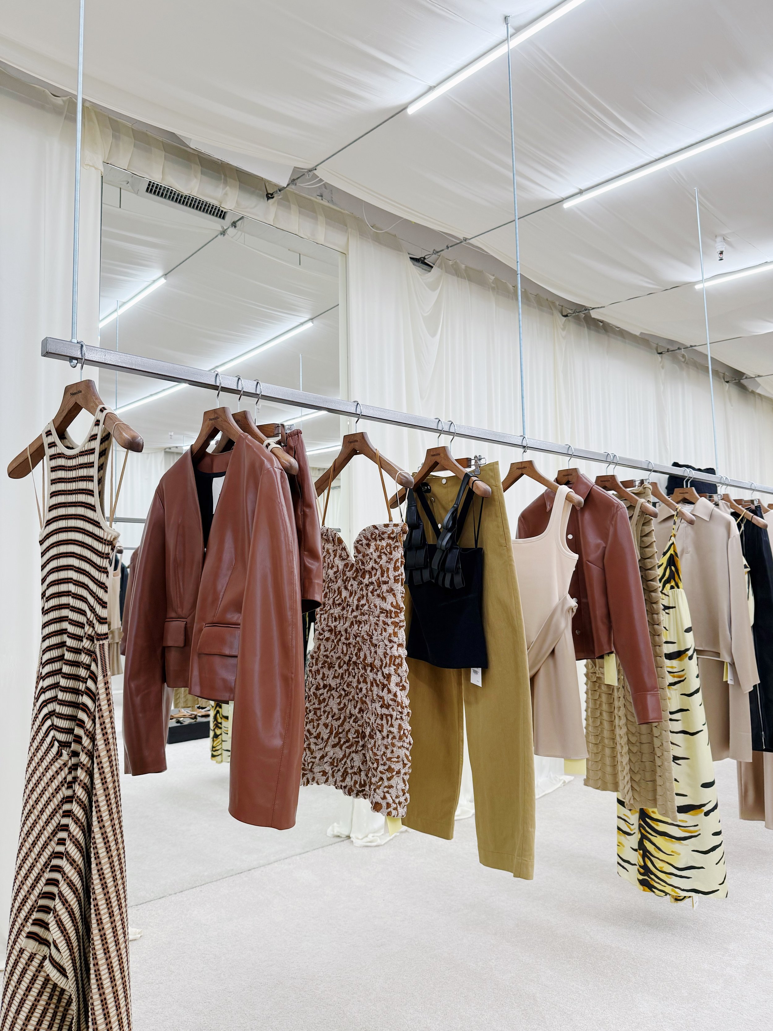 Clothing rack with dresses, jackets, and pants in various colors and patterns inside a retail store.