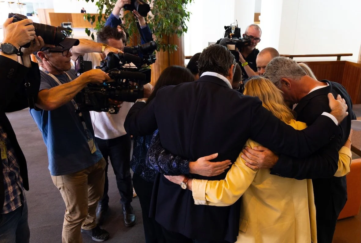 Group of people embracing in a tight hug while surrounded by photographers and cameramen.