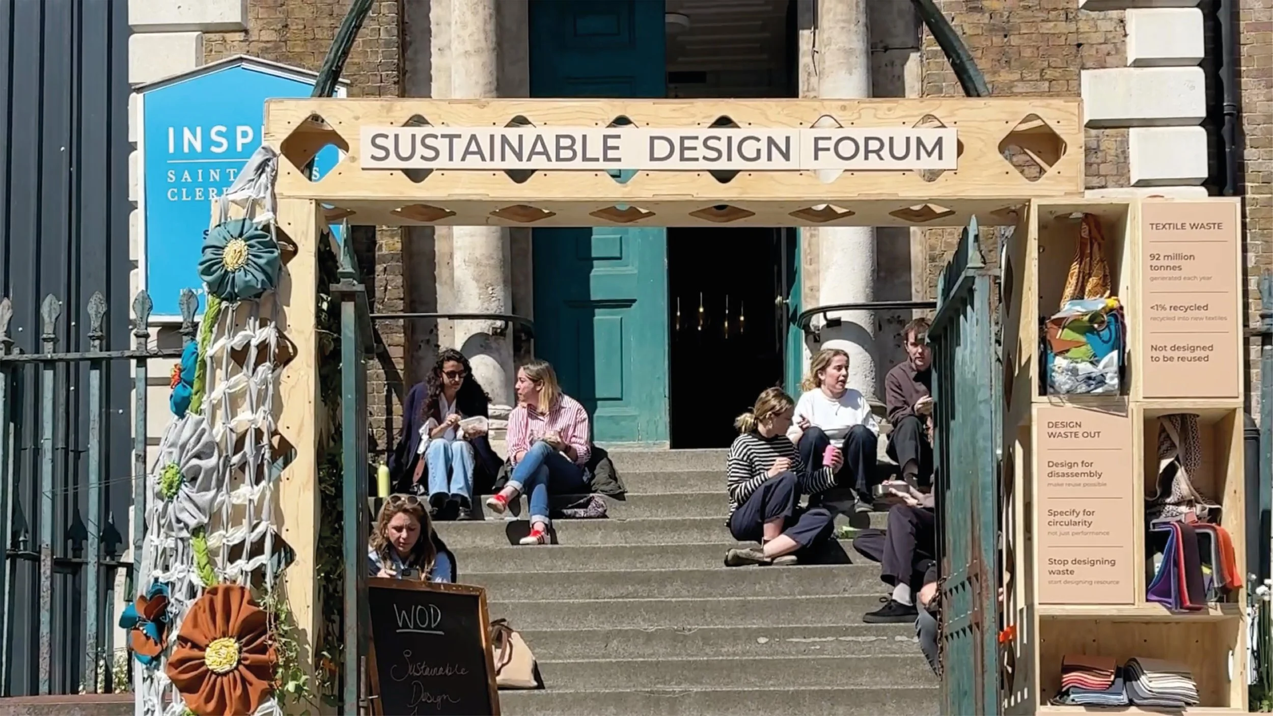 Sustainable Design Forum entrance at Saint Clement's London,  with visitors gathered on stone steps surrounded by upcycled  textile installations and circular design exhibits