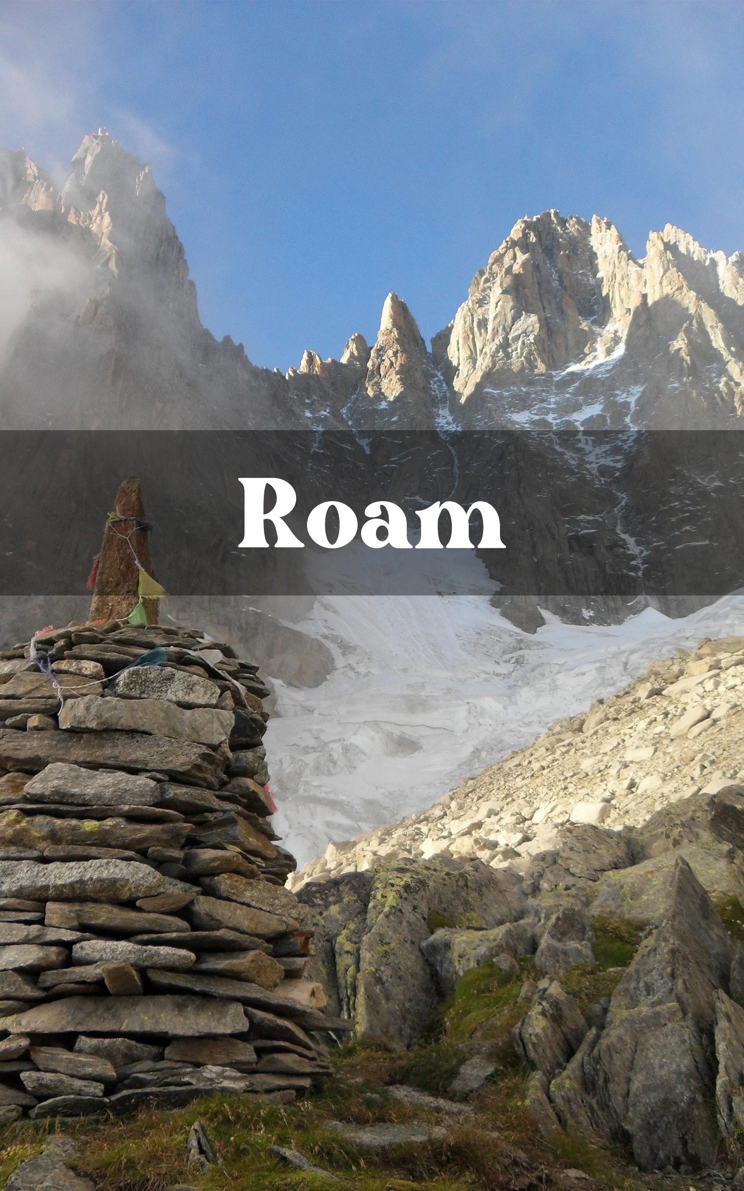 Snow-covered mountain peaks under a clear blue sky, with a stone cairn in the foreground and prayer flags attached to it.