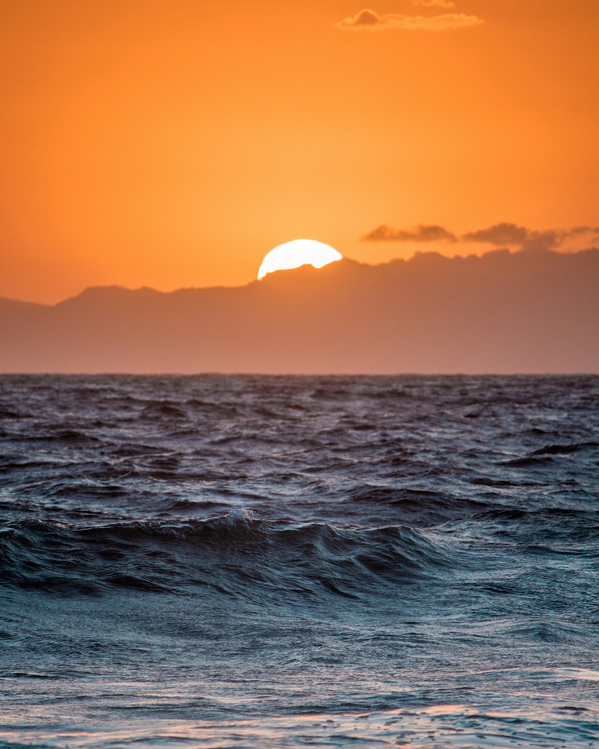 Sunset over the ocean with clouds in the sky and waves in the water.