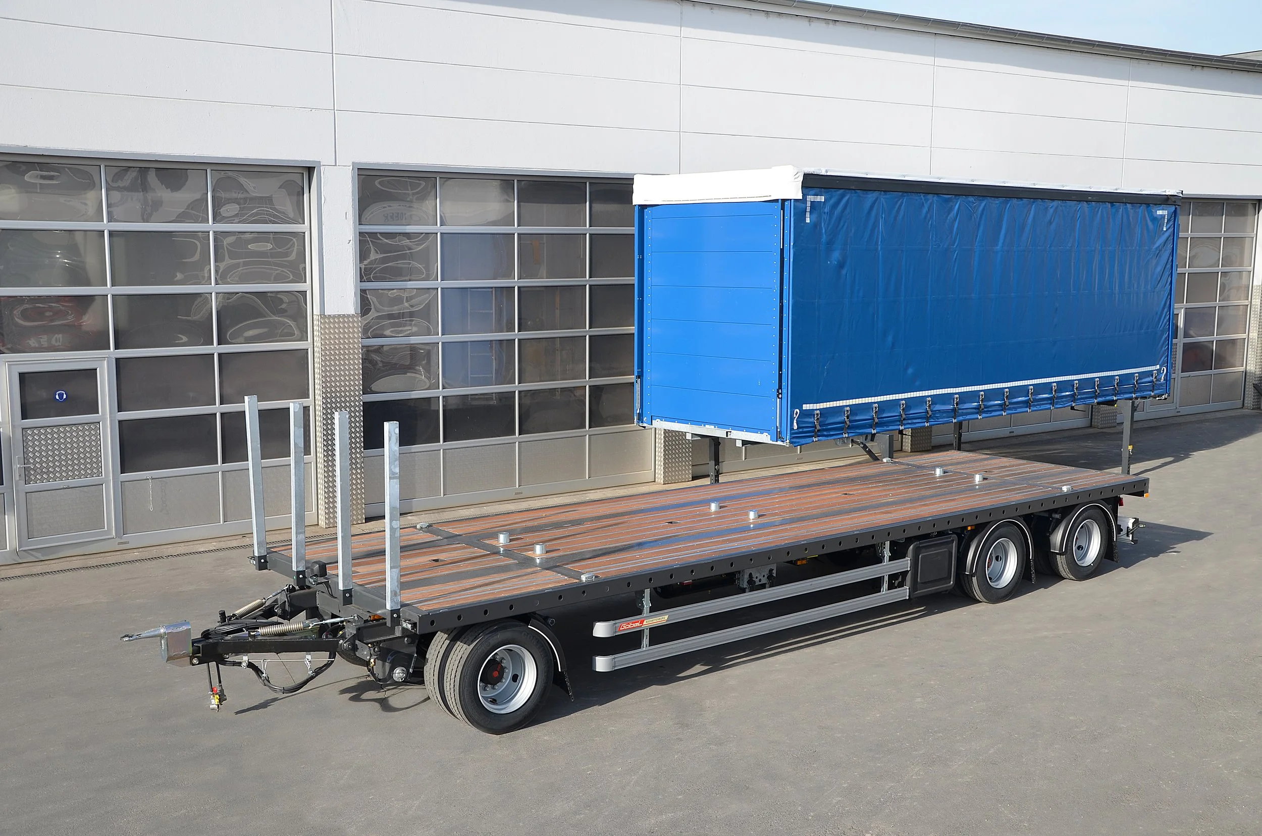 Ein LKW mit leerer Ladefläche und blauer Plane steht vor einem modernen Gebäude mit großen Fensterfronten.