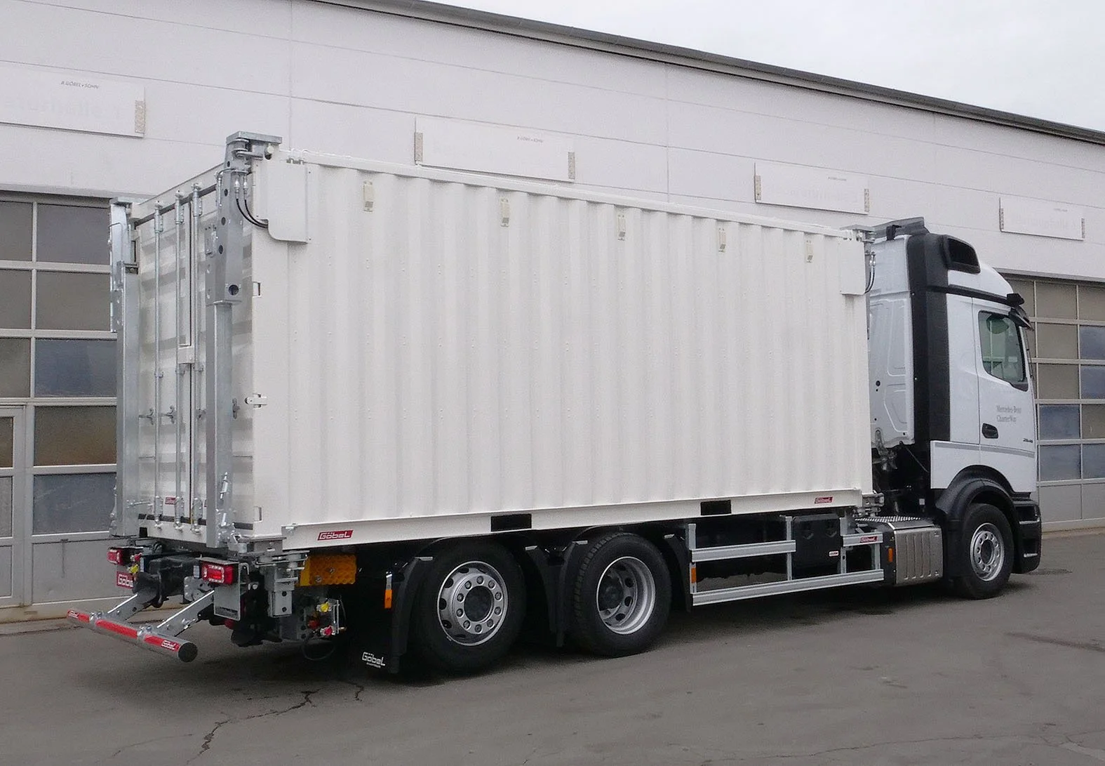 Weißer LKW mit einem großen, isolierten Container auf einem Gelände vor einer modernen Gebäudefassade.