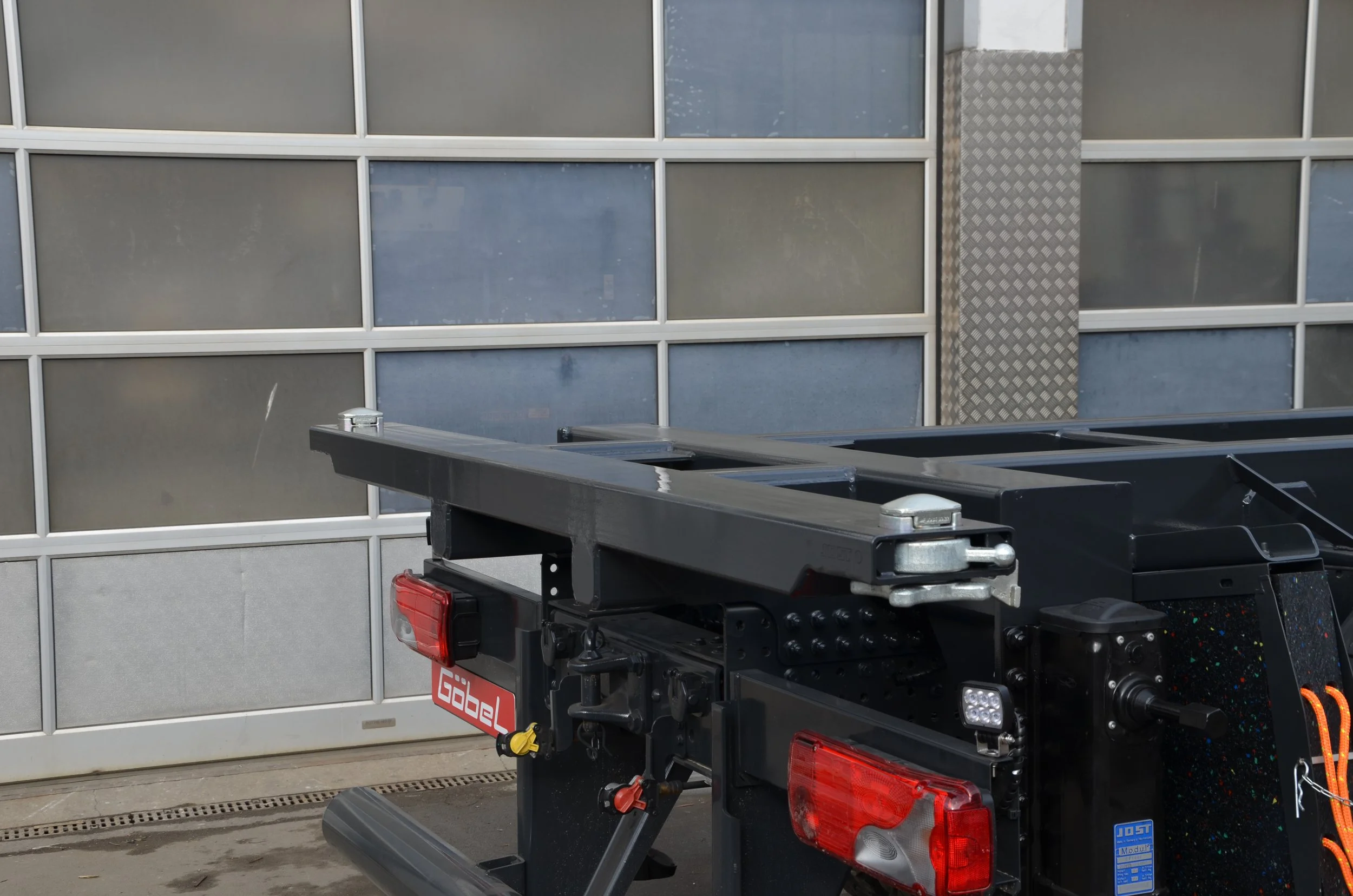Blick auf die Rückseite eines Trucks mit einer schwarzen Ladefläche, in der Nähe eines modernen Gebäudes mit großen Fensterflächen und einer metallischen Verkleidung.
