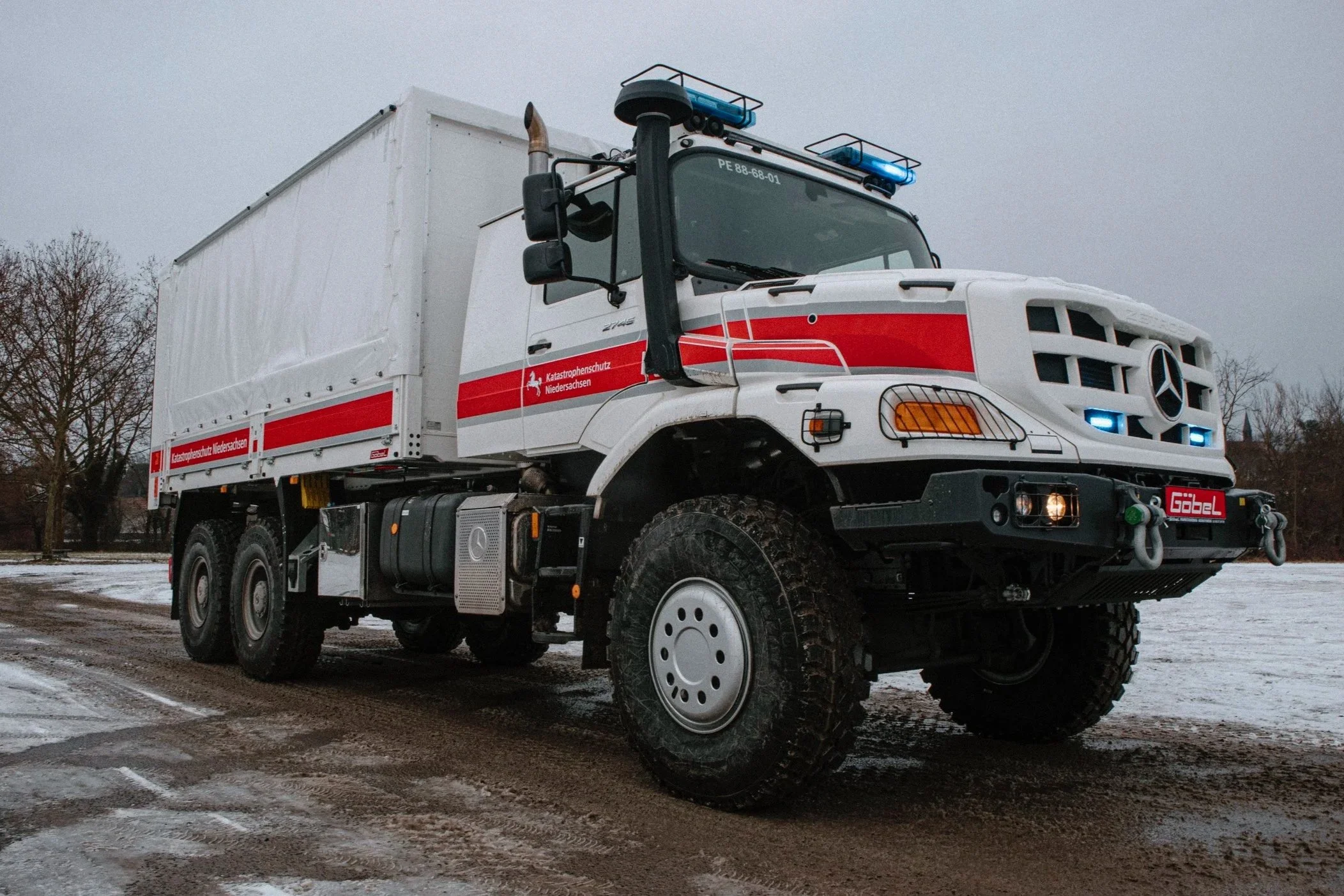 Ein weißer Rettungswagen mit blauen Lichtzeichen und roten Streifen, der auf einer schneebedeckten Straße steht. Der Wagen gehört zum Katastrophenschutz Niedersachsen.