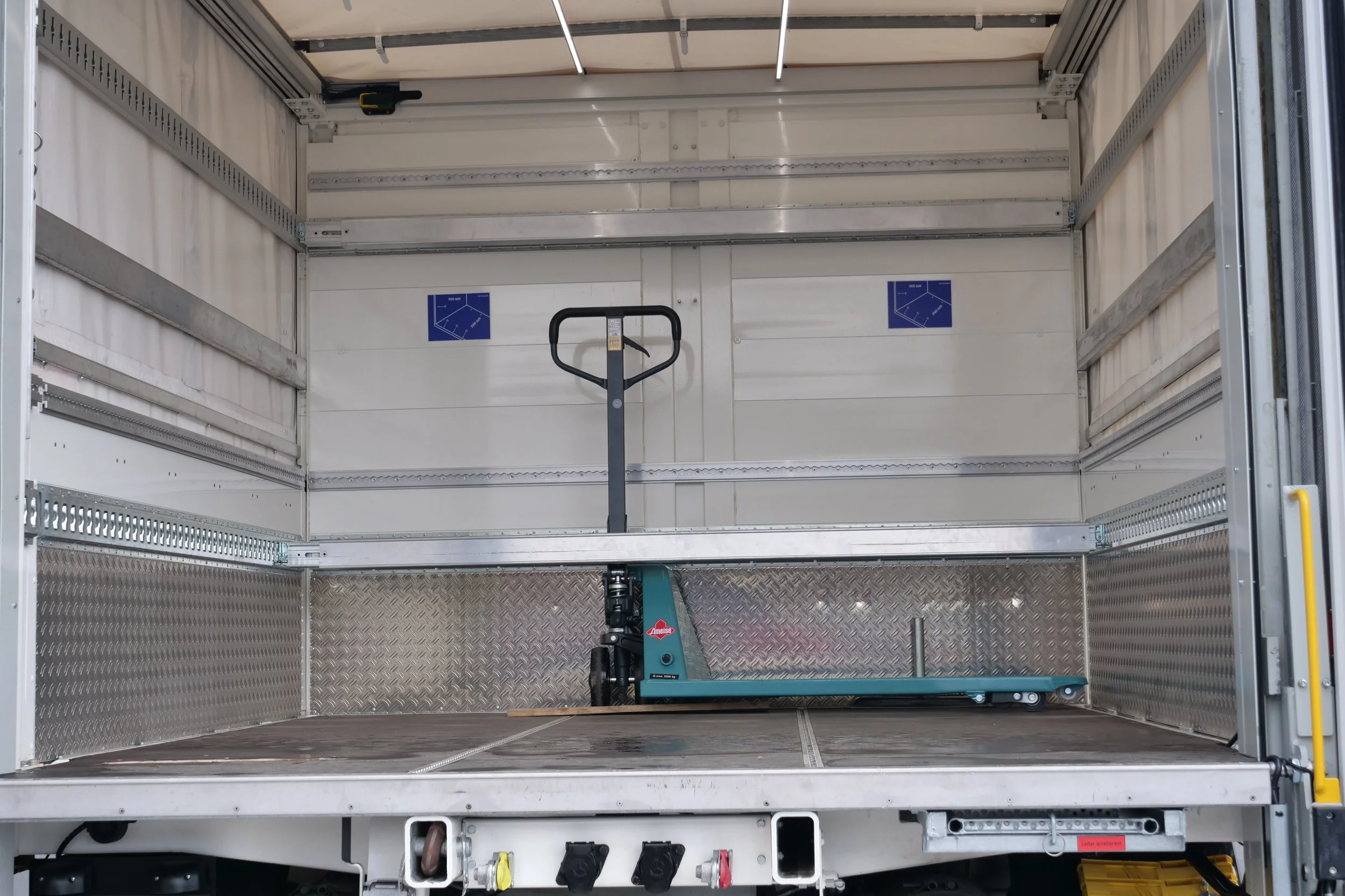 Innenansicht eines leeren LKW-Transporters mit einer Handhebeldämpfer und zwei blauen Hinweisschilder an der Rückwand.