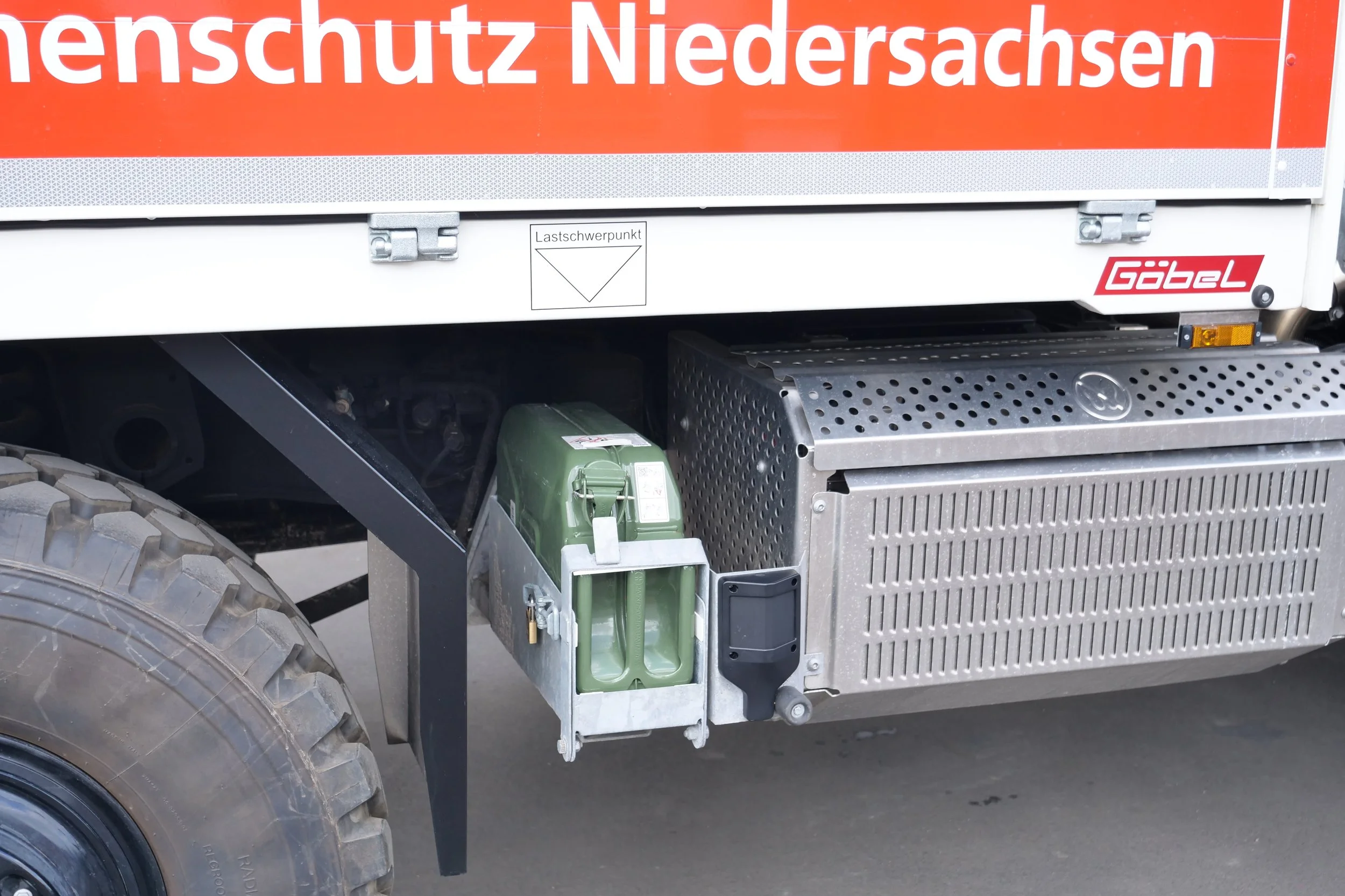 Ein Lastwagen mit einem großen roten und weißen Banner, auf dem 'Brandschutz Niedersachsen' steht. Der Lkw hat eine strukturierte Metallseite, eine grüne Flüssigkeitskanister und technische Komponenten. Das Bild zeigt einen Teil des Fahrzeugs, einsch