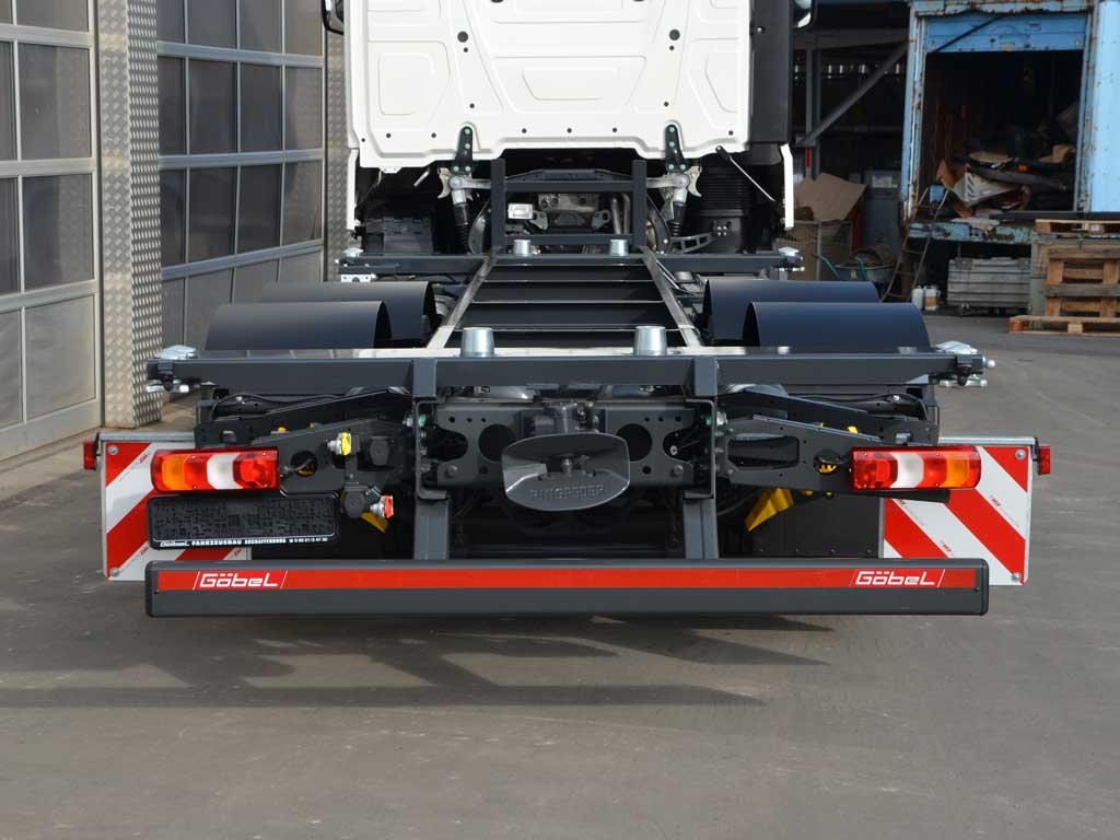 Leeres LKW-Chassis mit schwarzen Reifen und Reflektorstreifen auf dem Boden in einer Werkstatt.