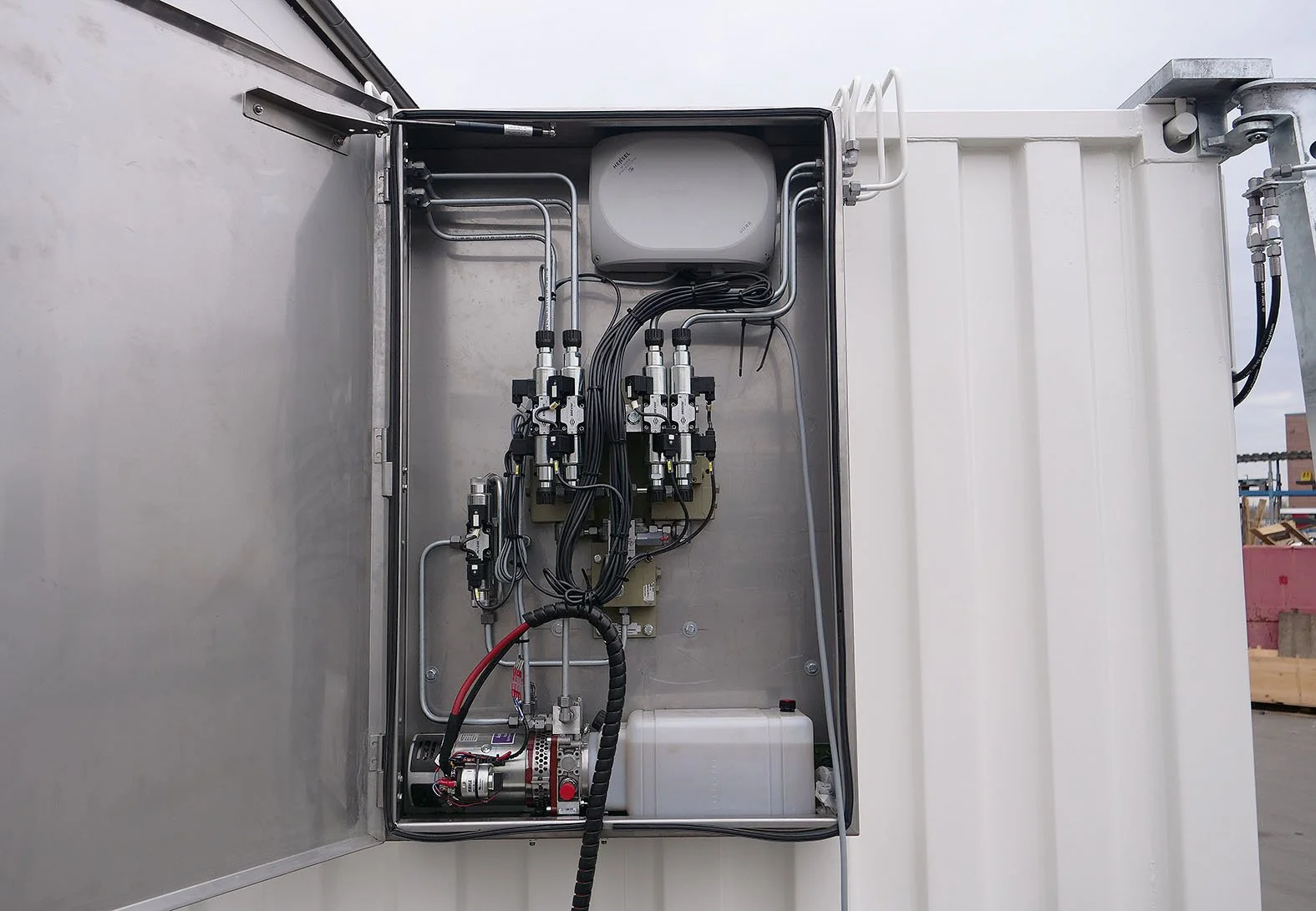 Innenansicht eines elektrischen Steuerungskastens mit Kabeln, Ventilen und elektronischen Komponenten, installiert auf einer Industrieanlage im Freien.