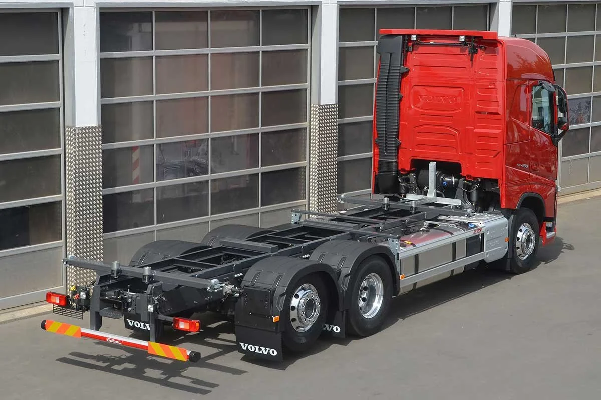 Ein roter Lastwagen ohne Auflieger, nur der Fahrerhaus, steht vor einer großen, modernen Garage.