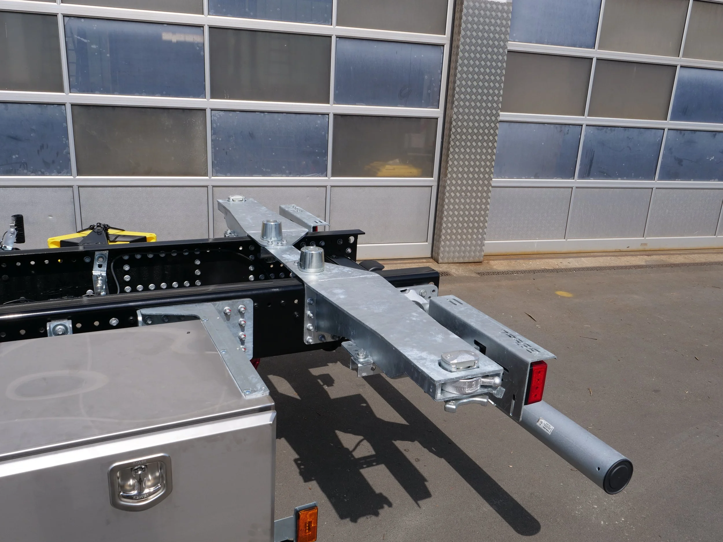 Ein LKW mit einer Anhängerkupplung und einer Metallplattform vor einem Gebäude mit Fenstern.