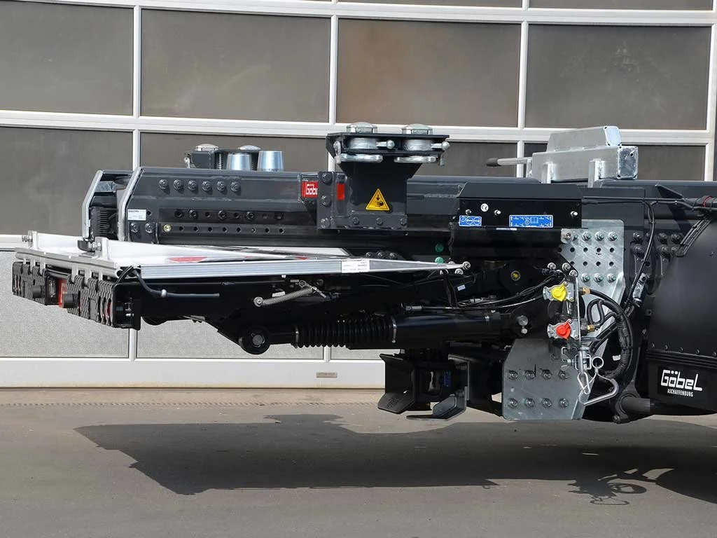 Nahaufnahme eines landwirtschaftlichen Anbaus an einem Fahrzeug, wahrscheinlich eines Mähdreschers, mit mechanischen und hydraulischen Komponenten.