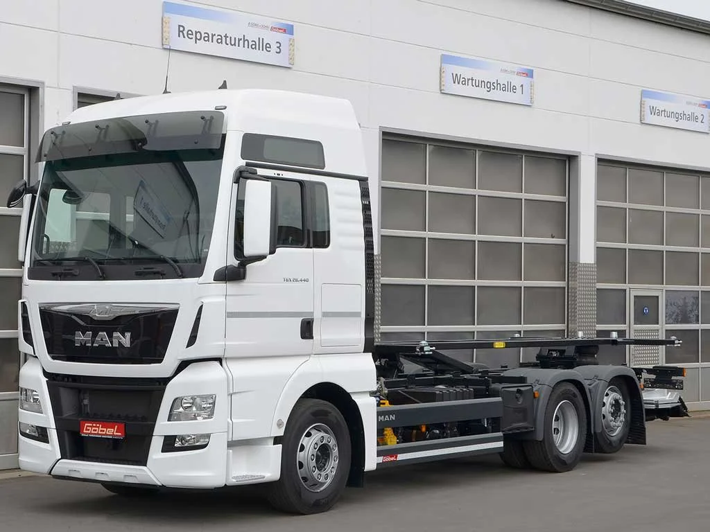 Ein weißes MAN-LKW ohne Auflieger vor einem Gebäude mit mehreren Schildern, die auf Reparatur- und Wartungshallen hinweisen.