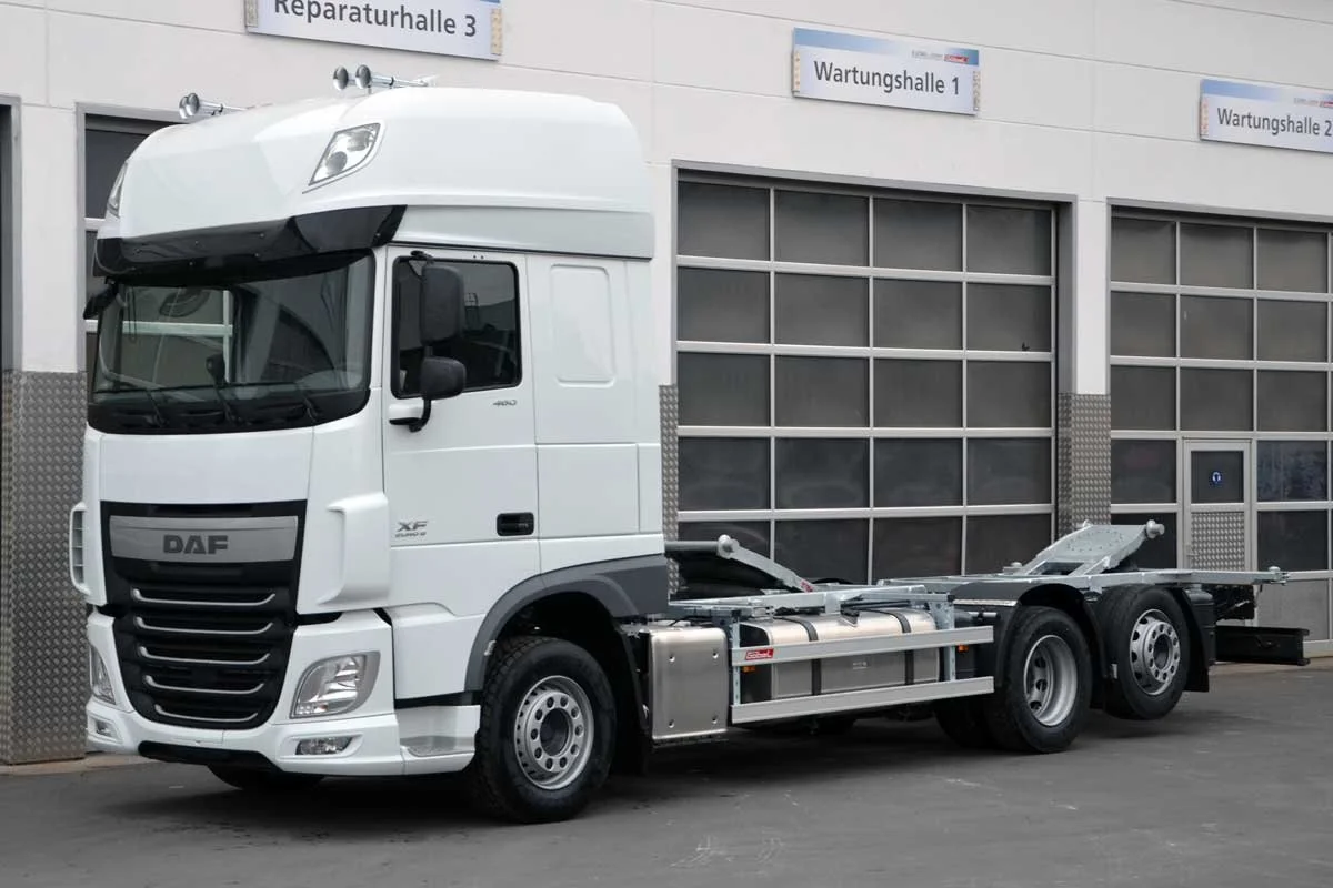Ein weißer Lkw ohne Auflieger vor einer Werkstatt mit Beschilderung für Reparatur- und Wartungshallen.
