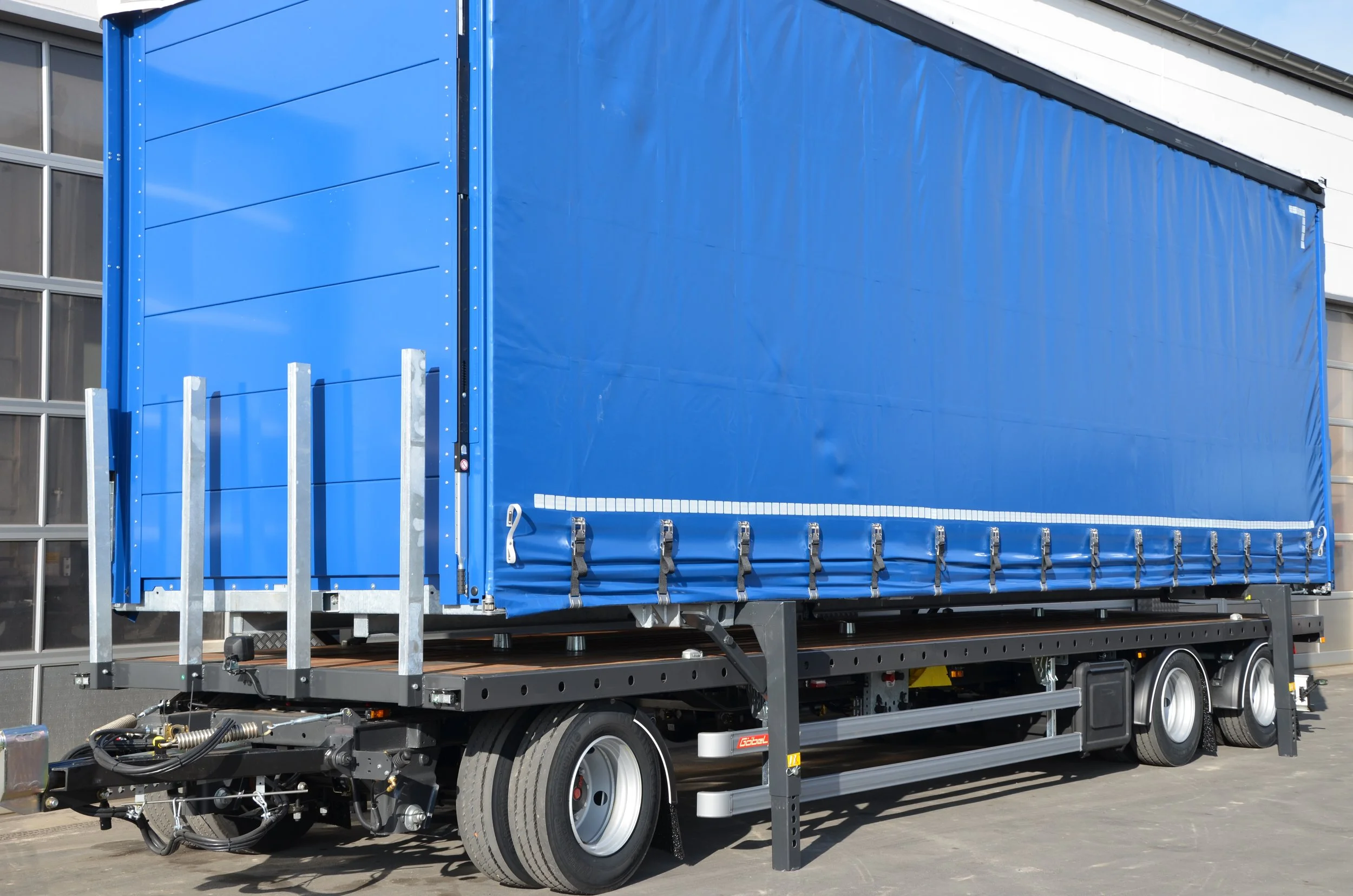 Ein blauer LKW mit eingerolltem Planenaufbau auf einem Carport in einer Industriehalle.
