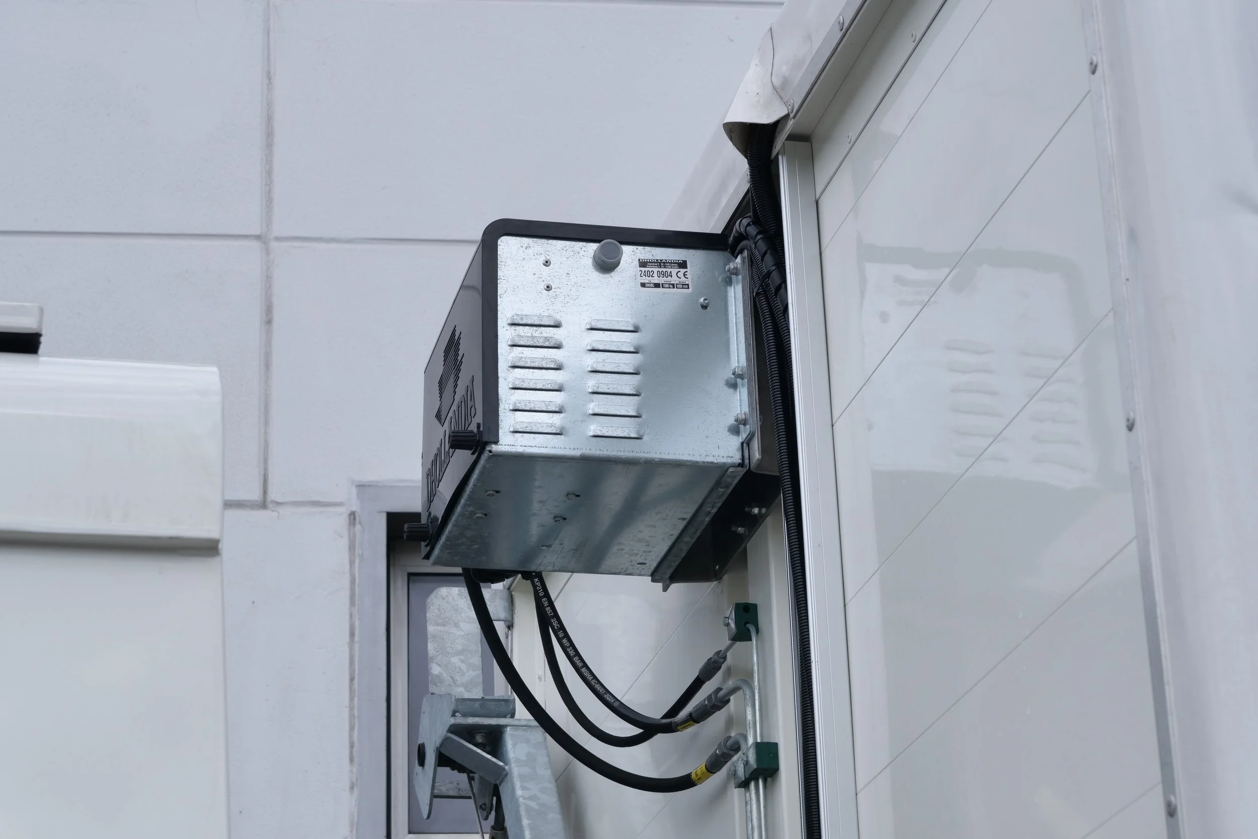 Installation von elektrischen Komponenten an einer weißen Wand mit sichtbaren Kabeln und Metallgehäusen.