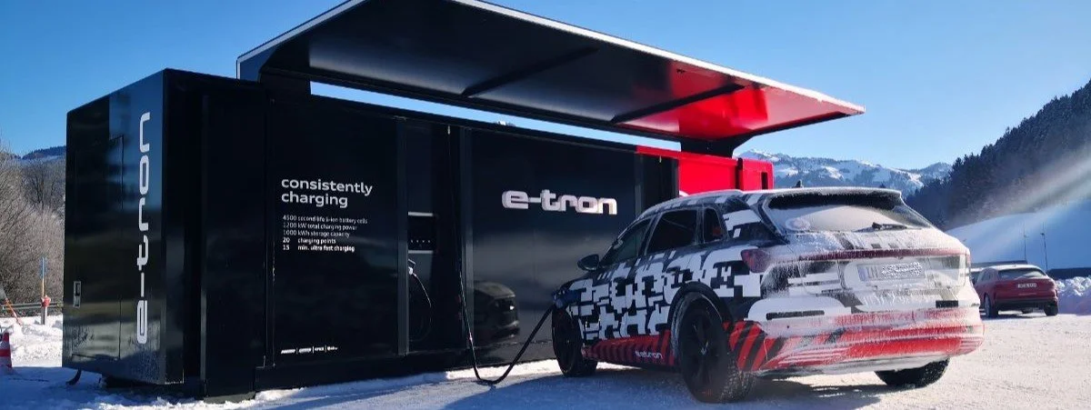 Ein E-Auto wird an eine mobile Ladestation in verschneiter Berglandschaft angeschlossen.