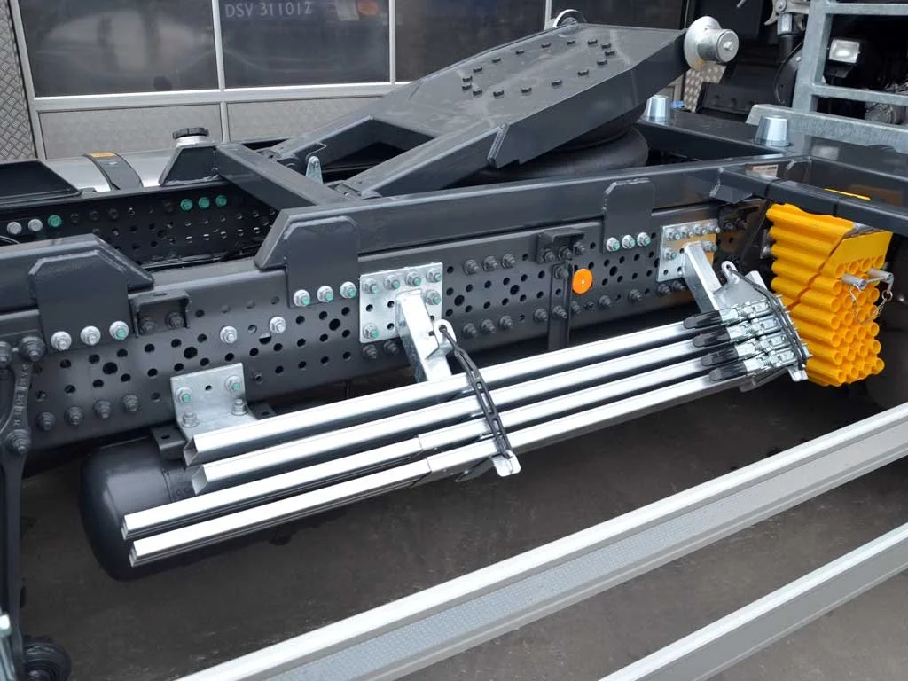 Blick auf eine technische Maschine mit verschiedenen metallischen Komponenten, darunter Schrauben, Rohre und gelbe Schutzabdeckungen, vermutlich ein Teil eines Fahrzeug- oder Werkzeugsystems