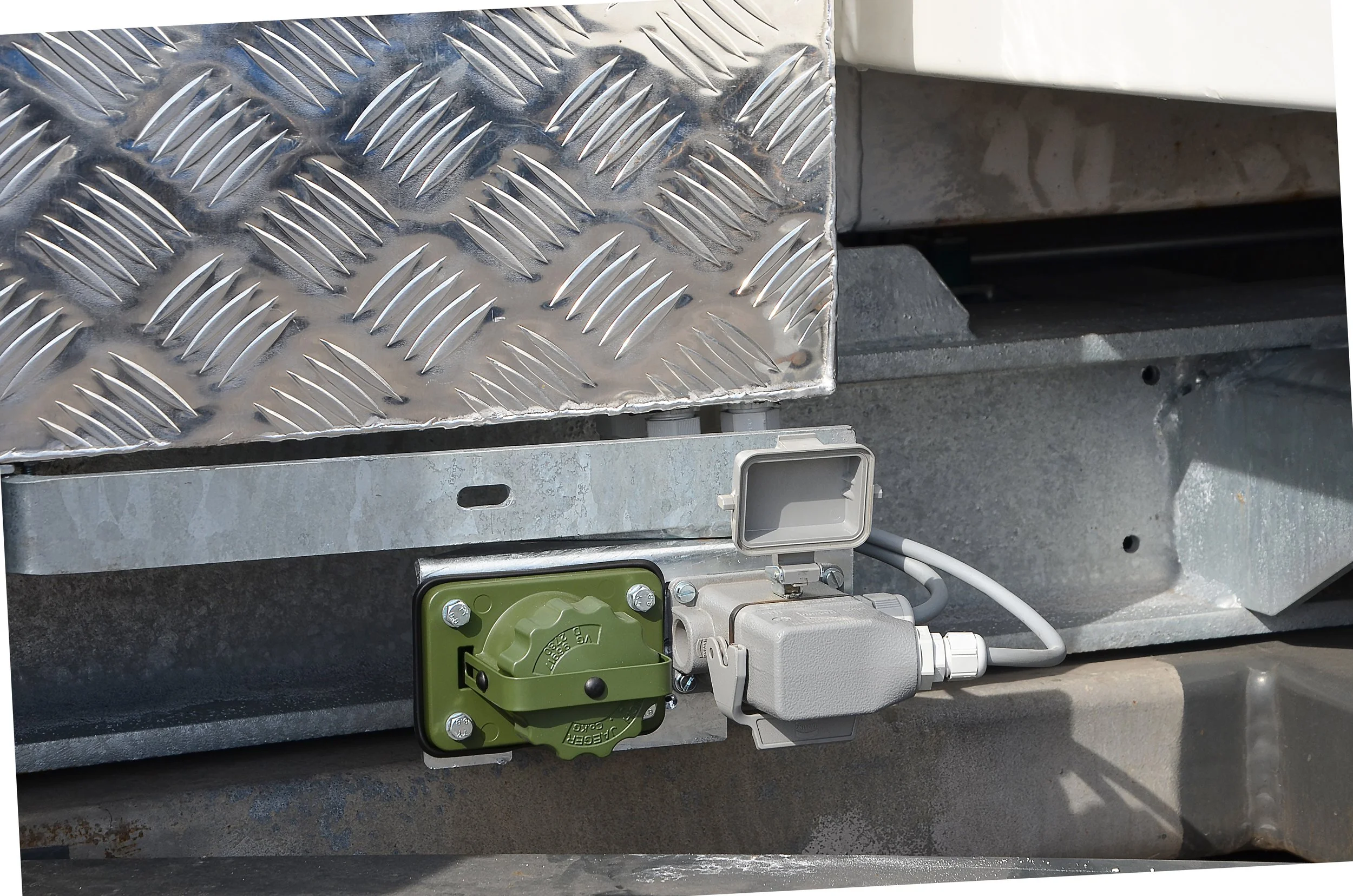 Nahaufnahme eines industriellen Geräts mit einer silbernen, gelochten Aluminiumplatte, verschiedenen elektrischen Komponenten, Kabeln und einem grünen mechanischen Teil.