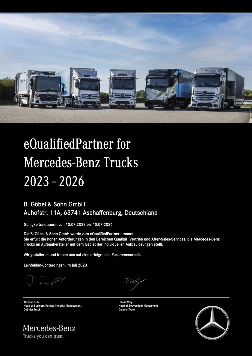 Mehrere Mercedes-Benz Lkw stehen auf einer Straße, der Himmel ist blau mit wenigen Wolken.