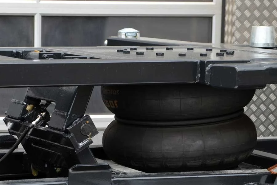 Nahaufnahme eines Flachbetts, das mit zwei großen schwarzen Reifen gestützt wird, auf einer Metallplattform, mit Steuerungselementen und Kabeln, im Hintergrund eine Fensterfront.