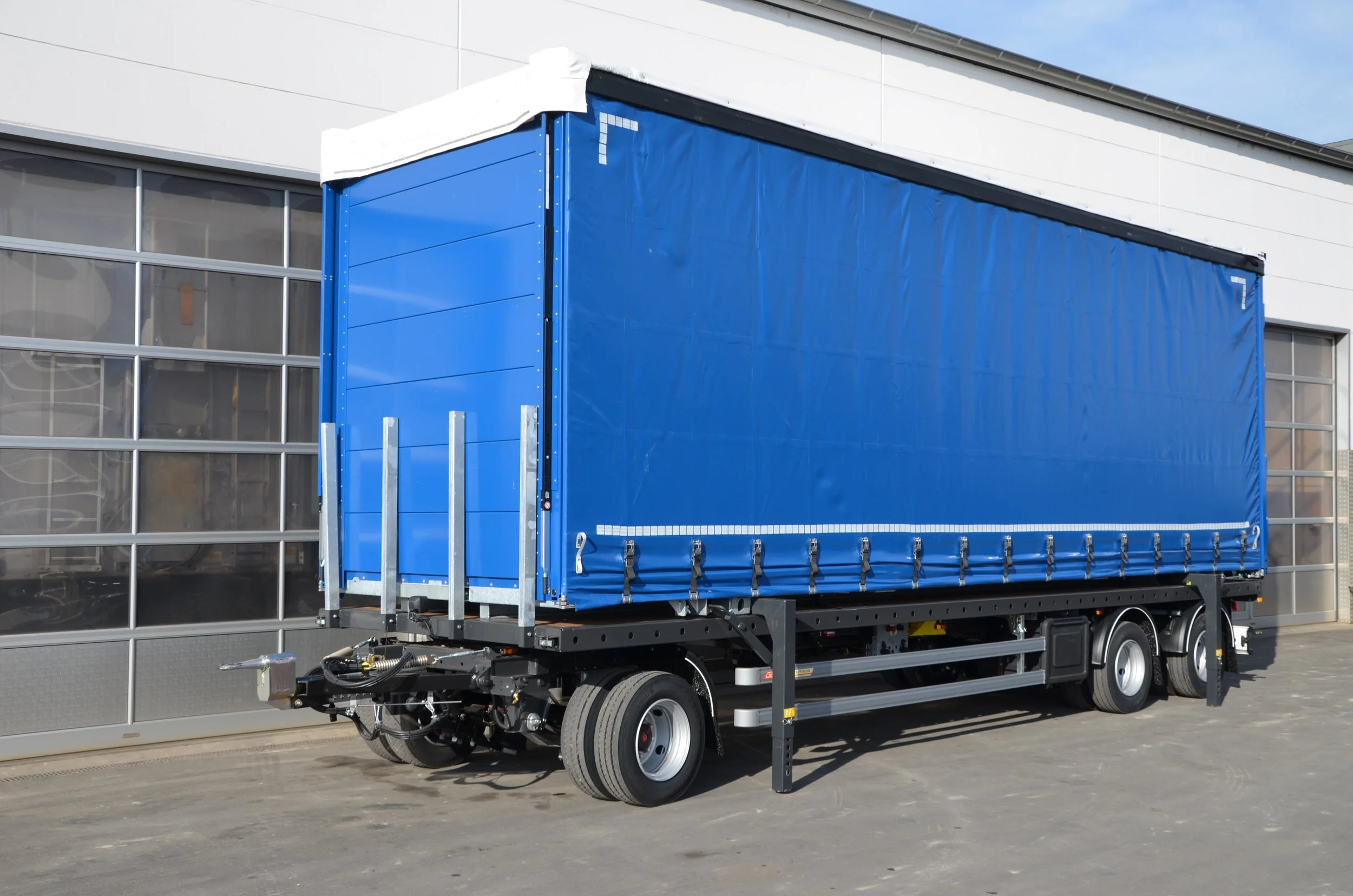 Ein blauer Lkw mit einem geschlossenen Planenaufsatz, der vor einem modernen Gebäude steht.