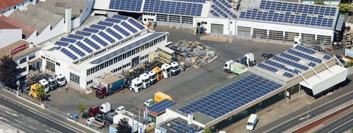 Büro- und Lagergebäude mit Solaranlagen auf den Dächern, in einem Industriegebiet mit mehreren Fahrzeugen und Lkw parkend.