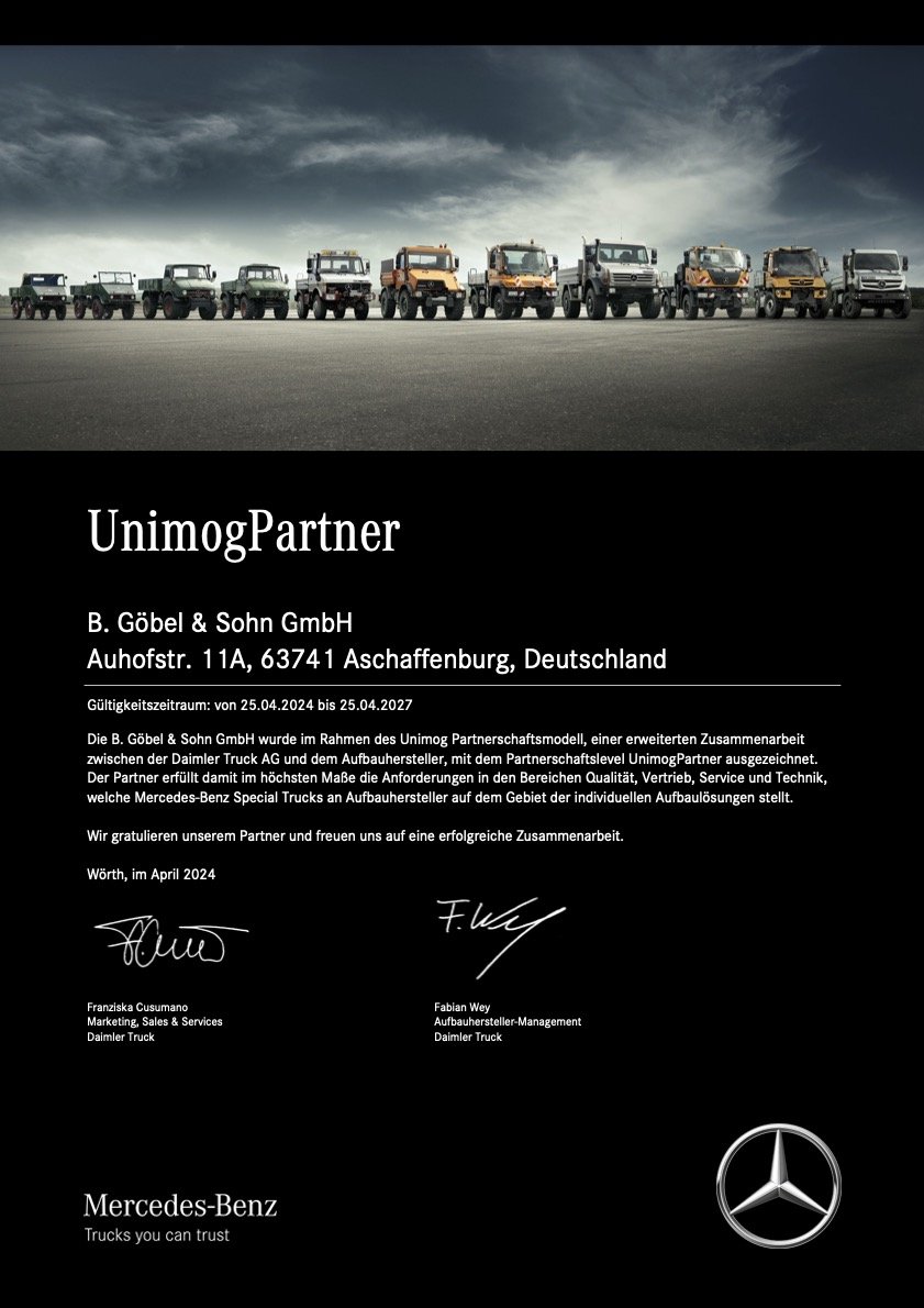 Eine Reihe von Mercedes-Benz Lastwagen und Pick-up-Fahrzeugen auf einer Straße, vor einem dunklen Himmel.